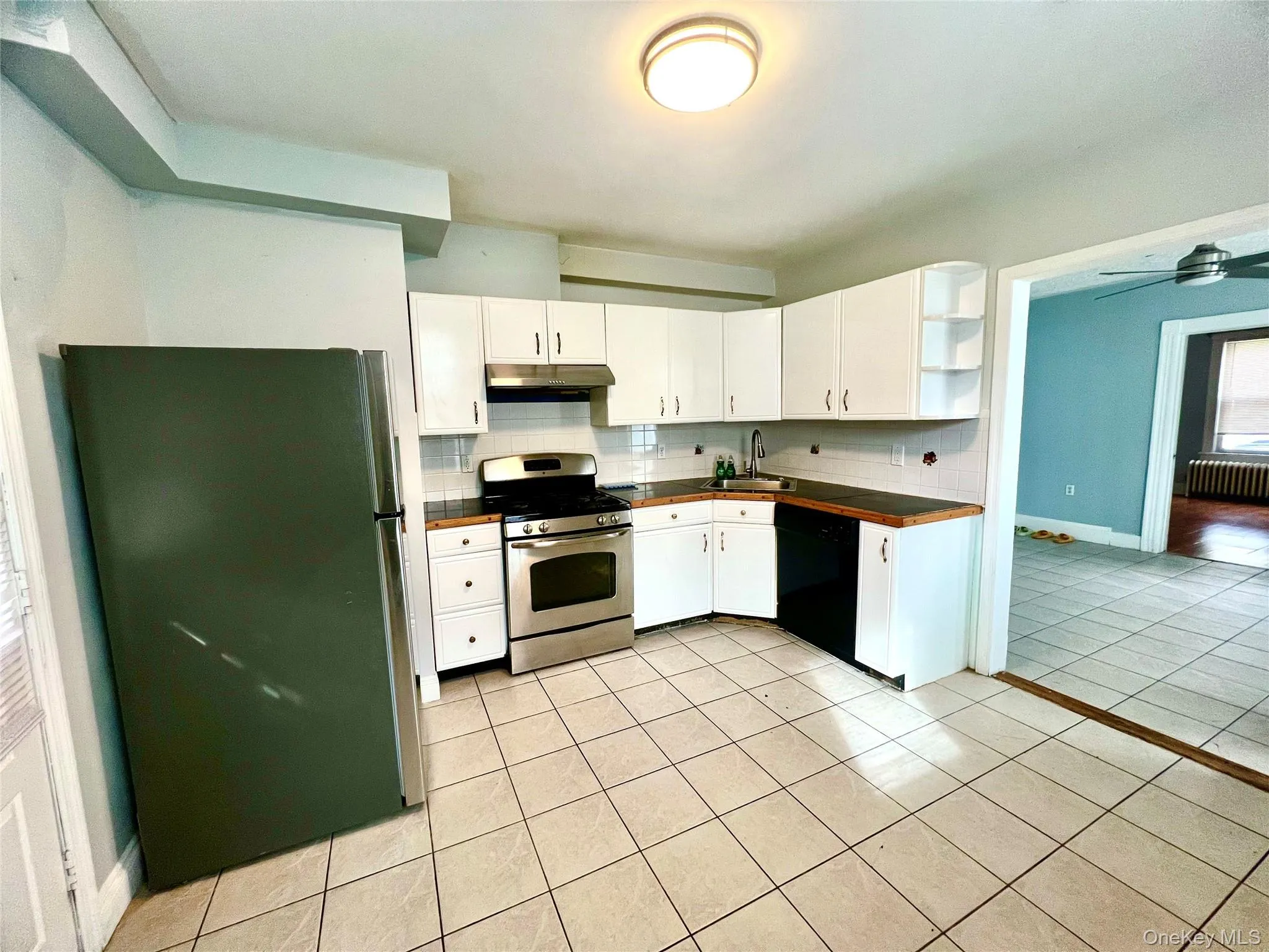 Kitchen featuring tasteful backsplash, stainless steel appliances, light tile patterned floors, open shelves, and white cabinets Kitchen featuring tasteful backsplash, stainless steel appliances, light tile patterned floors, open shelves, and white cabinets