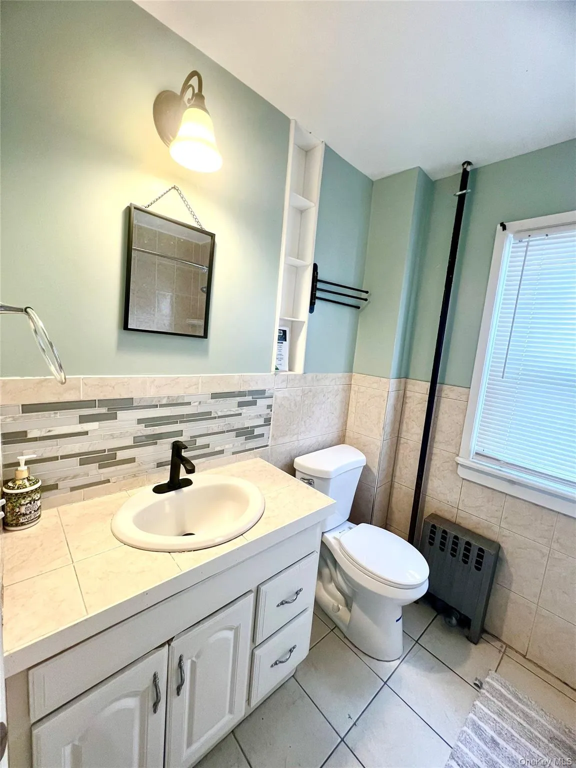 Full bath with radiator heating unit, light tile patterned flooring, vanity, tile walls, and a wainscoted wall Full bath with radiator heating unit, light tile patterned flooring, vanity, tile walls, and a wainscoted wall