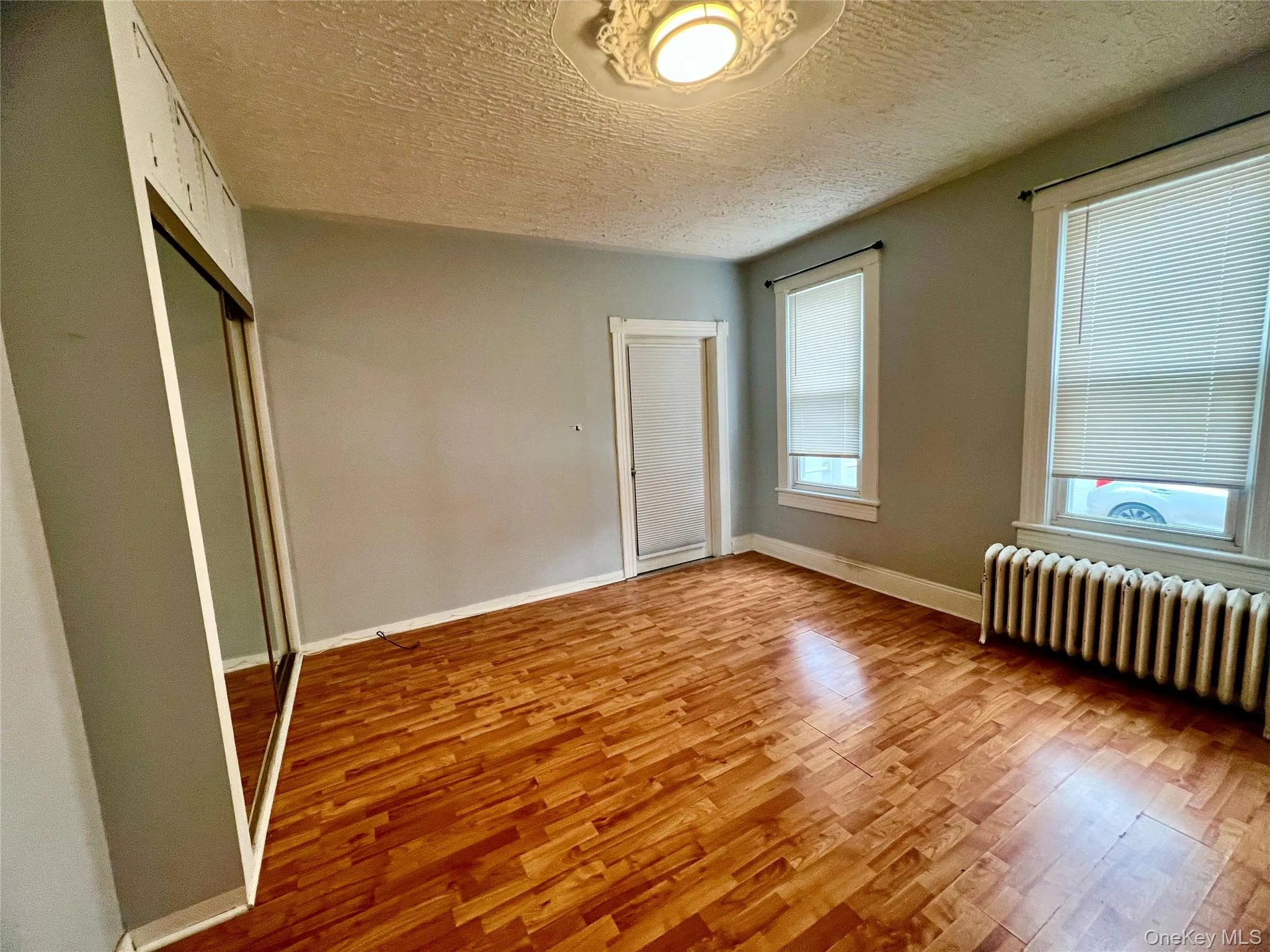 Unfurnished bedroom with light wood-type flooring, a closet, radiator, and a textured ceiling Unfurnished bedroom with light wood-type flooring, a closet, radiator, and a textured ceiling
