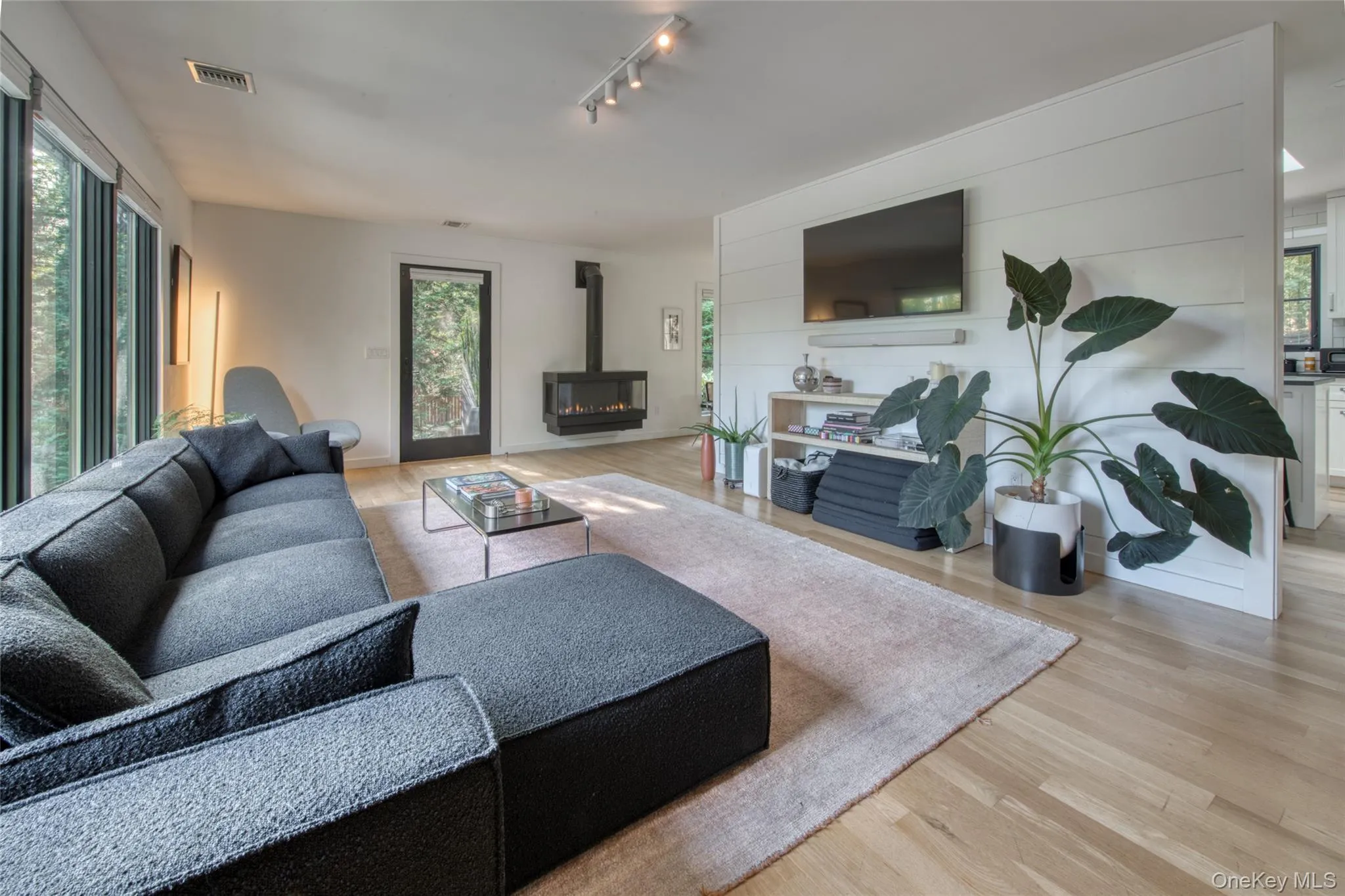 Living room featuring a wood stove, light wood-style floors, and rail lighting Living room featuring a wood stove, light wood-style floors, and rail lighting
