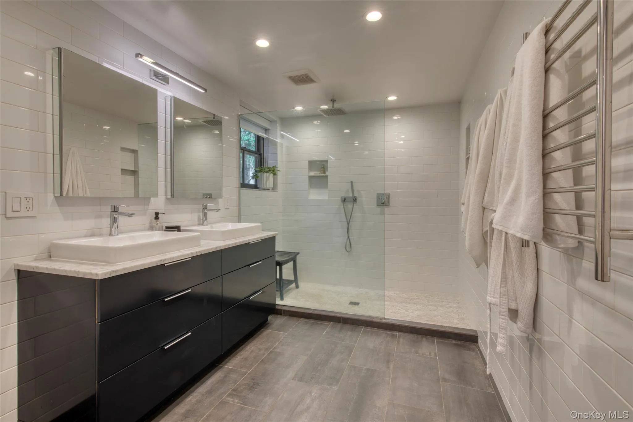 Full bathroom with a towel warming rack, tile walls, walk in shower, double vanity, and recessed lighting Full bathroom with a towel warming rack, tile walls, walk in shower, double vanity, and recessed lighting