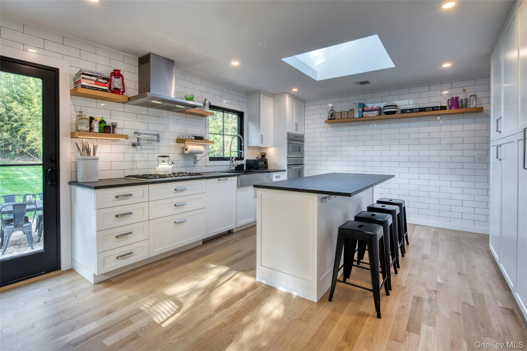 Kitchen featuring open shelves, a breakfast bar area, island exhaust hood, a skylight, and white cabinets Kitchen featuring open shelves, a breakfast bar area, island exhaust hood, a skylight, and white cabinets