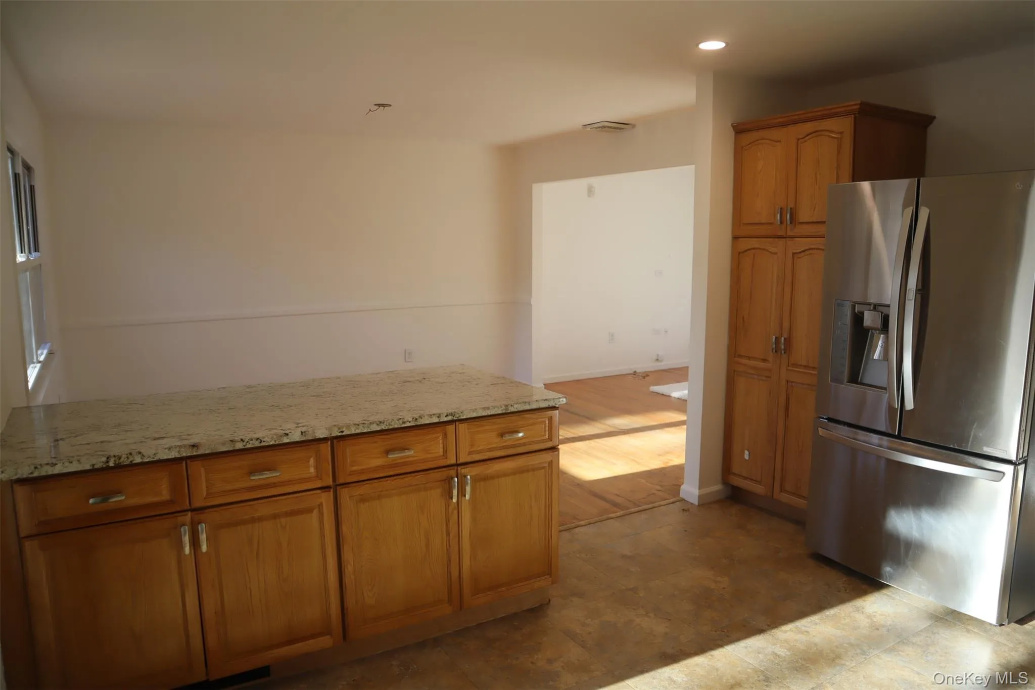 Kitchen with stainless steel refrigerator with ice dispenser, brown cabinetry, light stone countertops, and recessed lighting Kitchen with stainless steel refrigerator with ice dispenser, brown cabinetry, light stone countertops, and recessed lighting