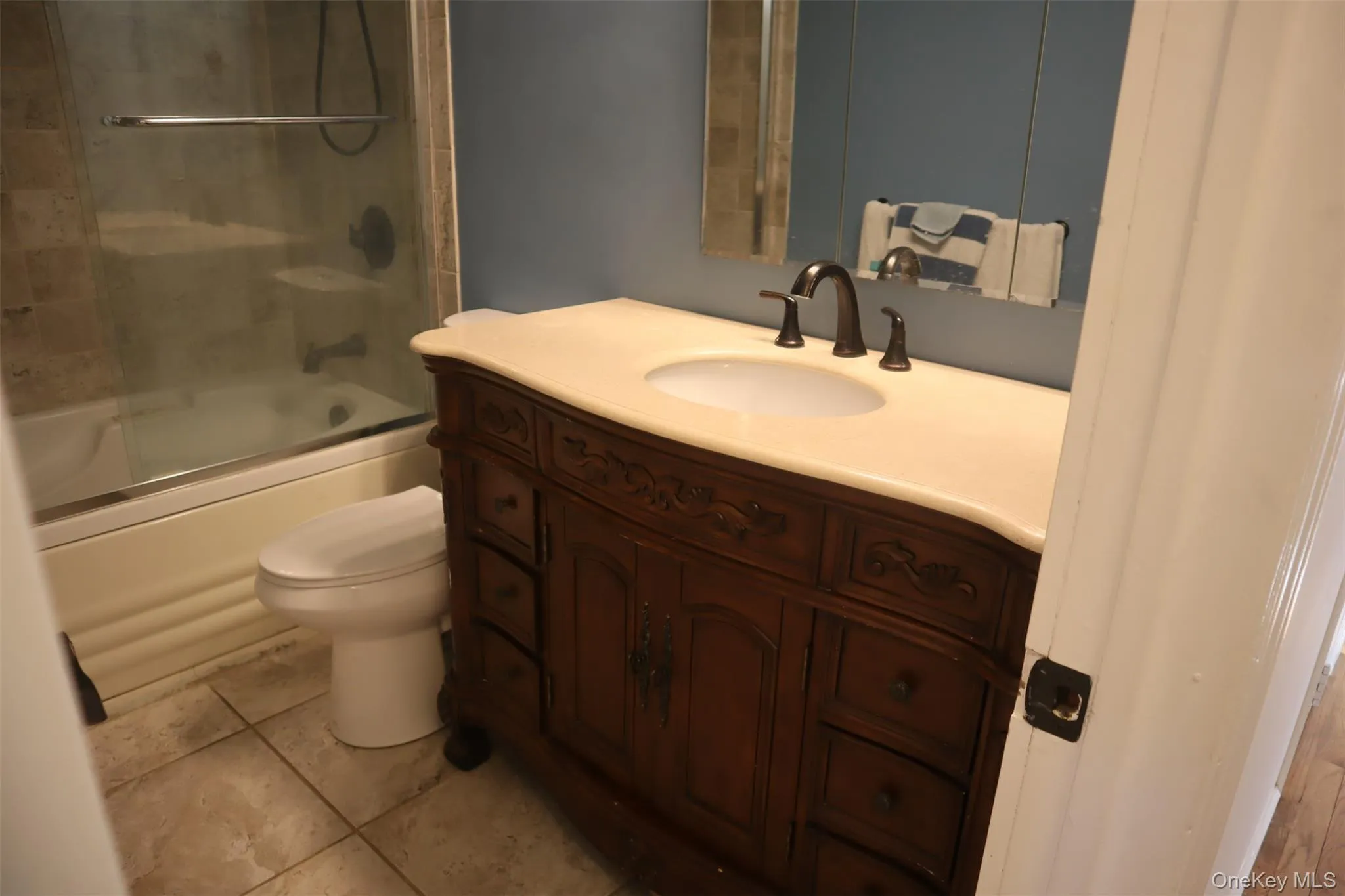 Full bath featuring vanity, shower / bath combination with glass door, and light tile patterned floors Full bath featuring vanity, shower / bath combination with glass door, and light tile patterned floors