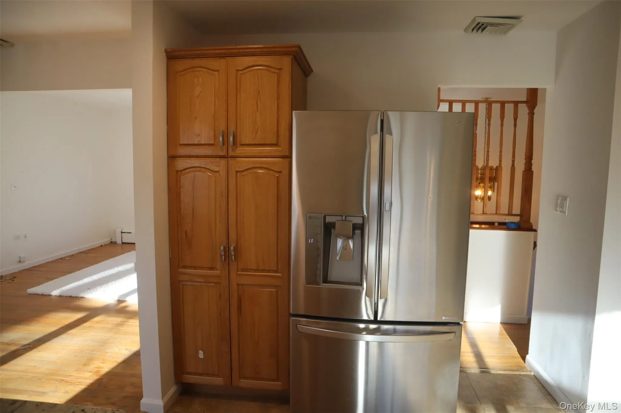 Kitchen featuring stainless steel fridge, brown cabinetry, dark wood-type flooring, and a baseboard radiator Kitchen featuring stainless steel fridge, brown cabinetry, dark wood-type flooring, and a baseboard radiator