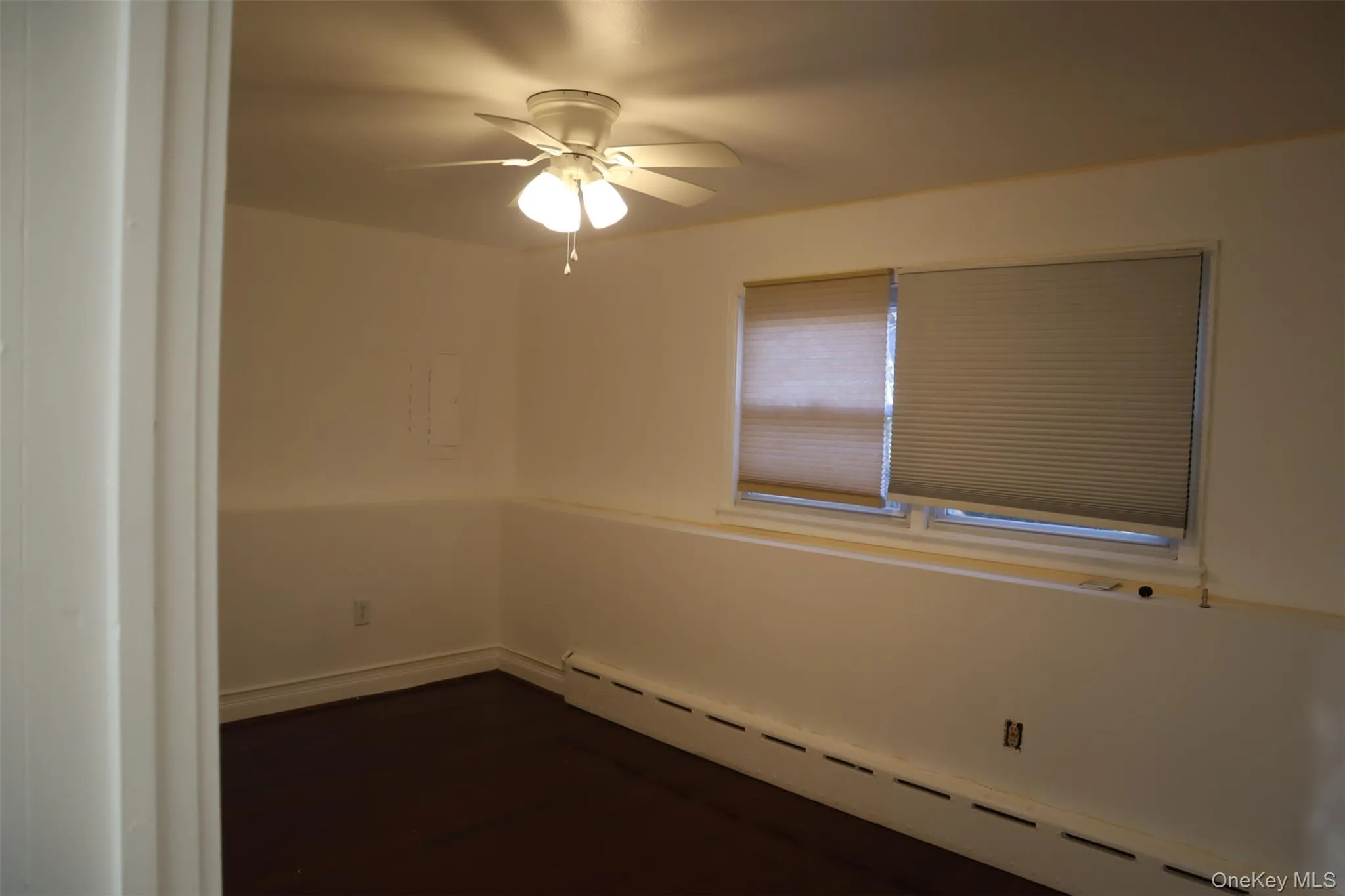 Empty room with a baseboard radiator, dark wood finished floors, and a ceiling fan Empty room with a baseboard radiator, dark wood finished floors, and a ceiling fan