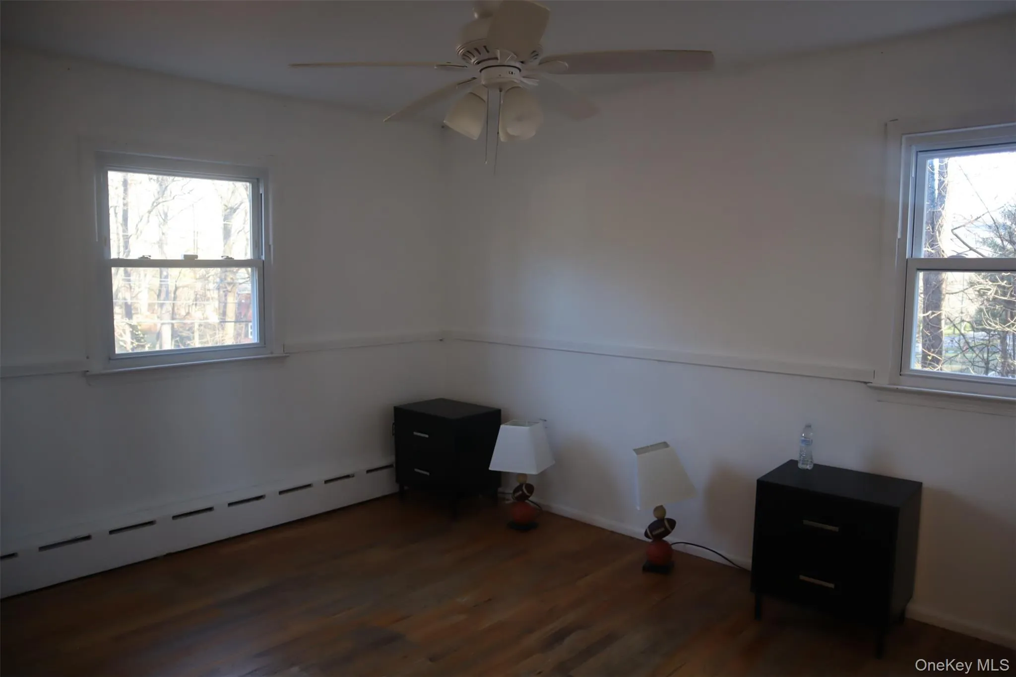 Unfurnished room featuring baseboard heating, dark wood-type flooring, healthy amount of natural light, and a ceiling fan Unfurnished room featuring baseboard heating, dark wood-type flooring, healthy amount of natural light, and a ceiling fan
