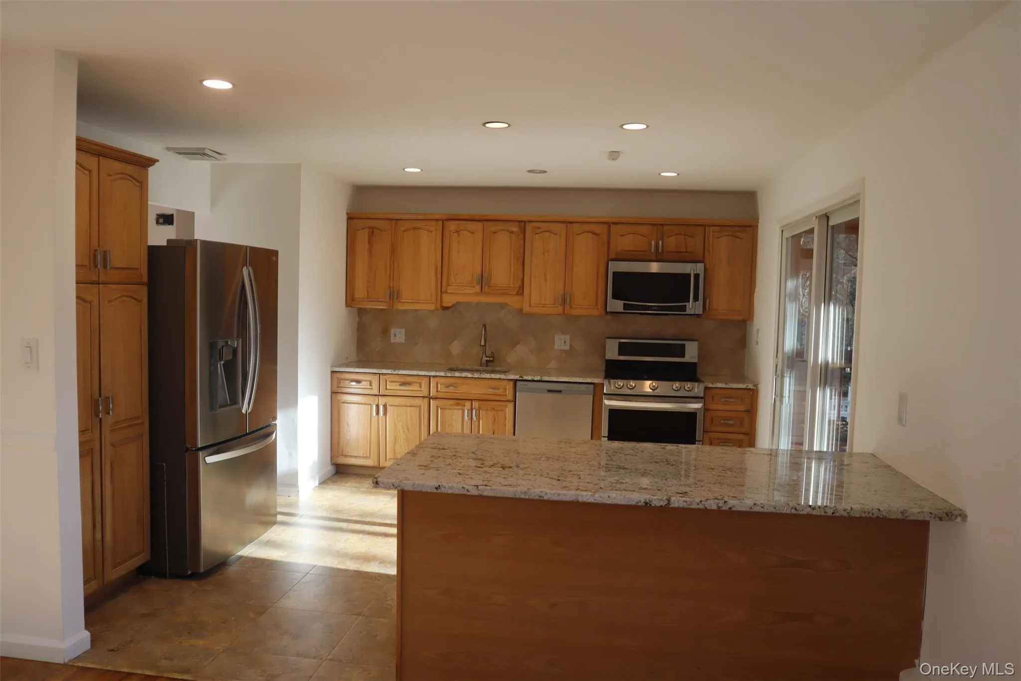 Kitchen with stainless steel appliances, light stone counters, brown cabinetry, a peninsula, and recessed lighting Kitchen with stainless steel appliances, light stone counters, brown cabinetry, a peninsula, and recessed lighting