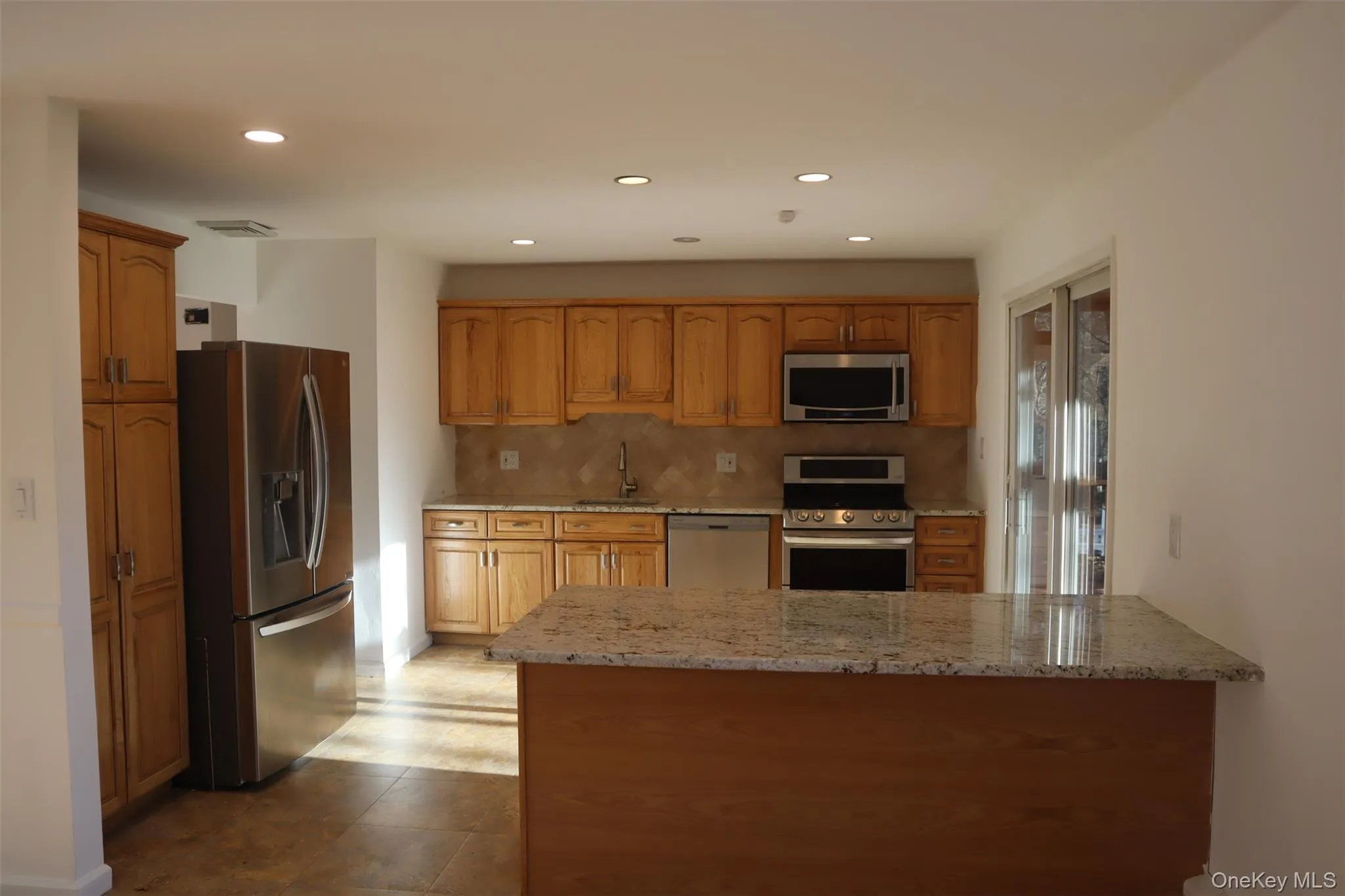 Kitchen with appliances with stainless steel finishes, brown cabinets, decorative backsplash, light stone counters, and a peninsula Kitchen with appliances with stainless steel finishes, brown cabinets, decorative backsplash, light stone counters, and a peninsula