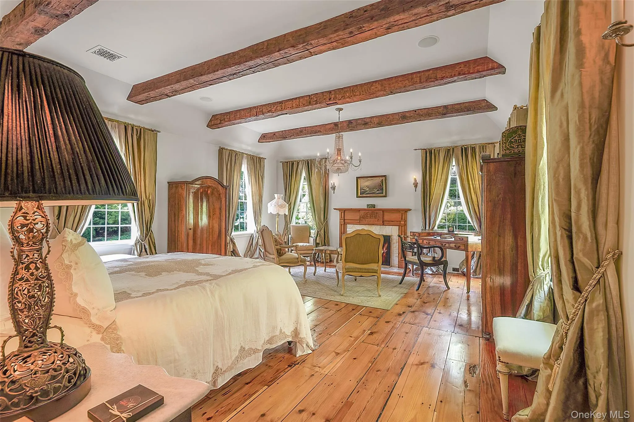 Bedroom featuring beam ceiling, multiple windows, a fireplace, hardwood / wood-style floors, and a chandelier Bedroom featuring beam ceiling, multiple windows, a fireplace, hardwood / wood-style floors, and a chandelier