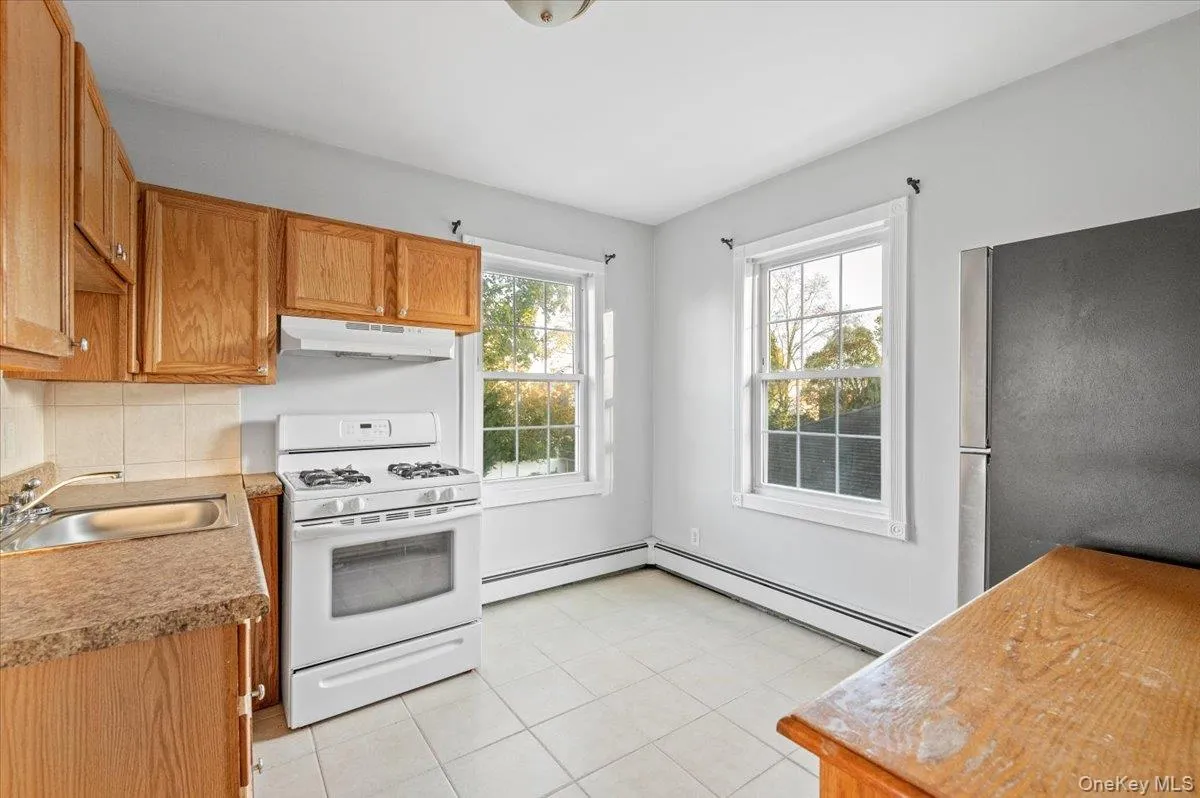 Kitchen featuring white gas range, freestanding refrigerator, light tile patterned floors, under cabinet range hood, and tasteful backsplash Kitchen featuring white gas range, freestanding refrigerator, light tile patterned floors, under cabinet range hood, and tasteful backsplash