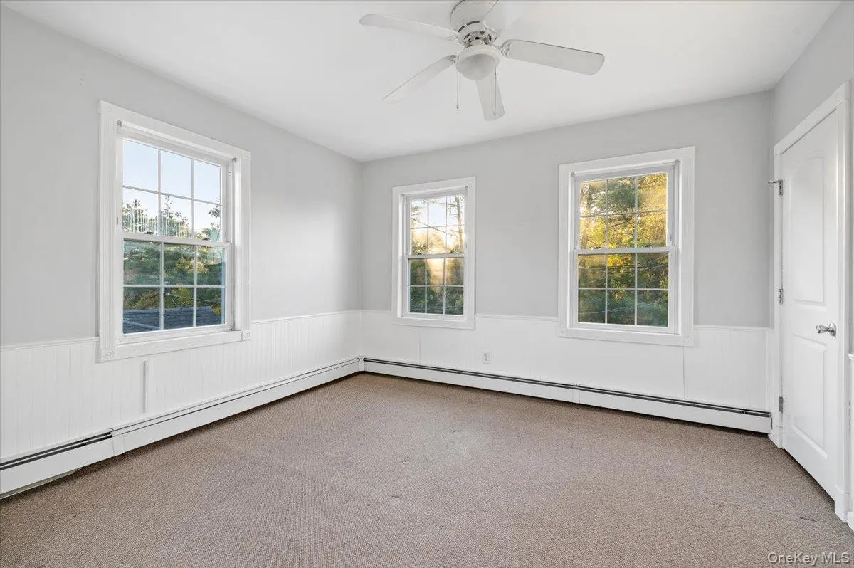 Carpeted spare room featuring wainscoting, a baseboard heating unit, and a ceiling fan Carpeted spare room featuring wainscoting, a baseboard heating unit, and a ceiling fan