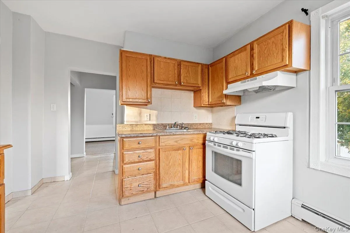Kitchen with gas range gas stove, a baseboard radiator, light countertops, under cabinet range hood, and light tile patterned floors Kitchen with gas range gas stove, a baseboard radiator, light countertops, under cabinet range hood, and light tile patterned floors