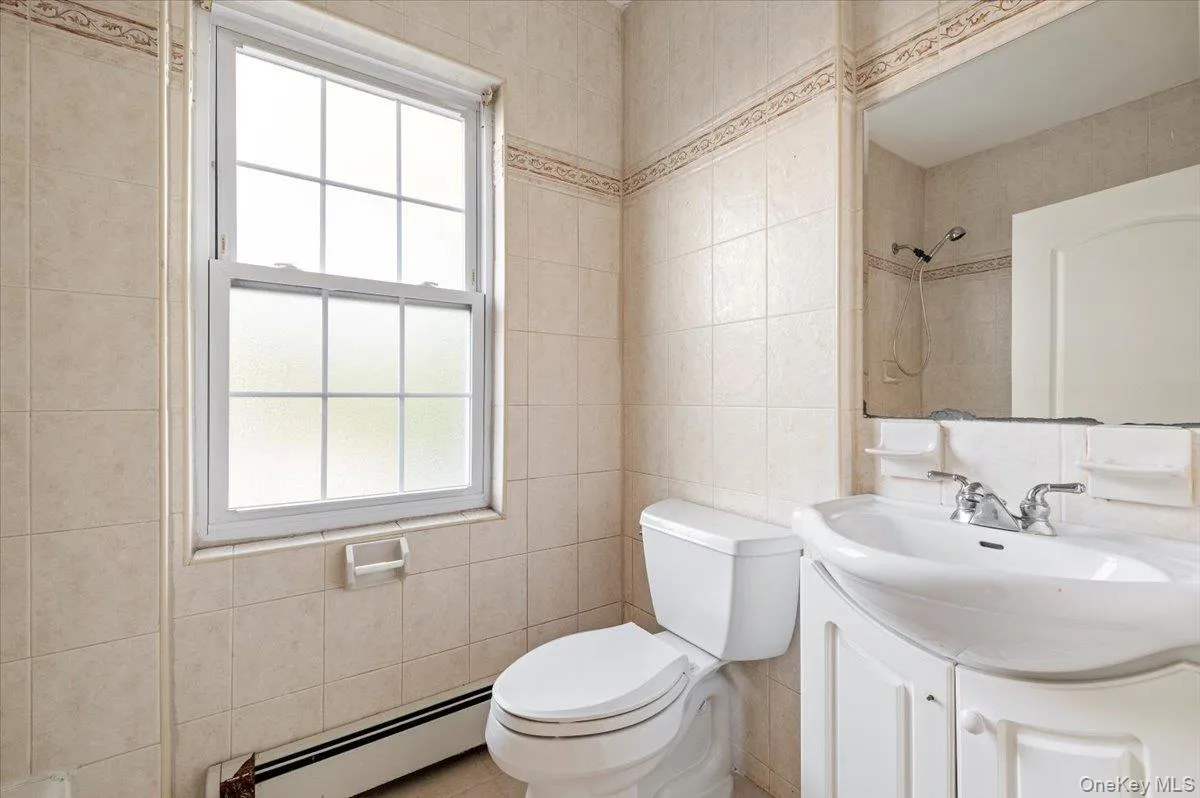 Full bathroom with tile walls, a baseboard heating unit, vanity, and a shower Full bathroom with tile walls, a baseboard heating unit, vanity, and a shower