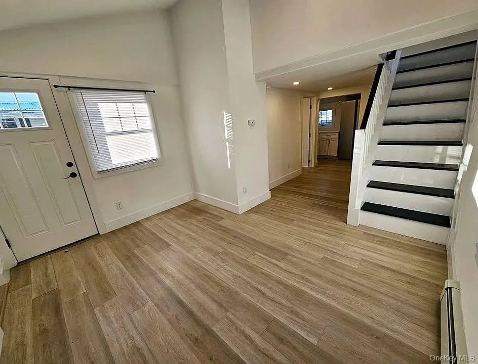 Foyer featuring stairs, light wood-type flooring, lofted ceiling, baseboard heating, and recessed lighting Foyer featuring stairs, light wood-type flooring, lofted ceiling, baseboard heating, and recessed lighting