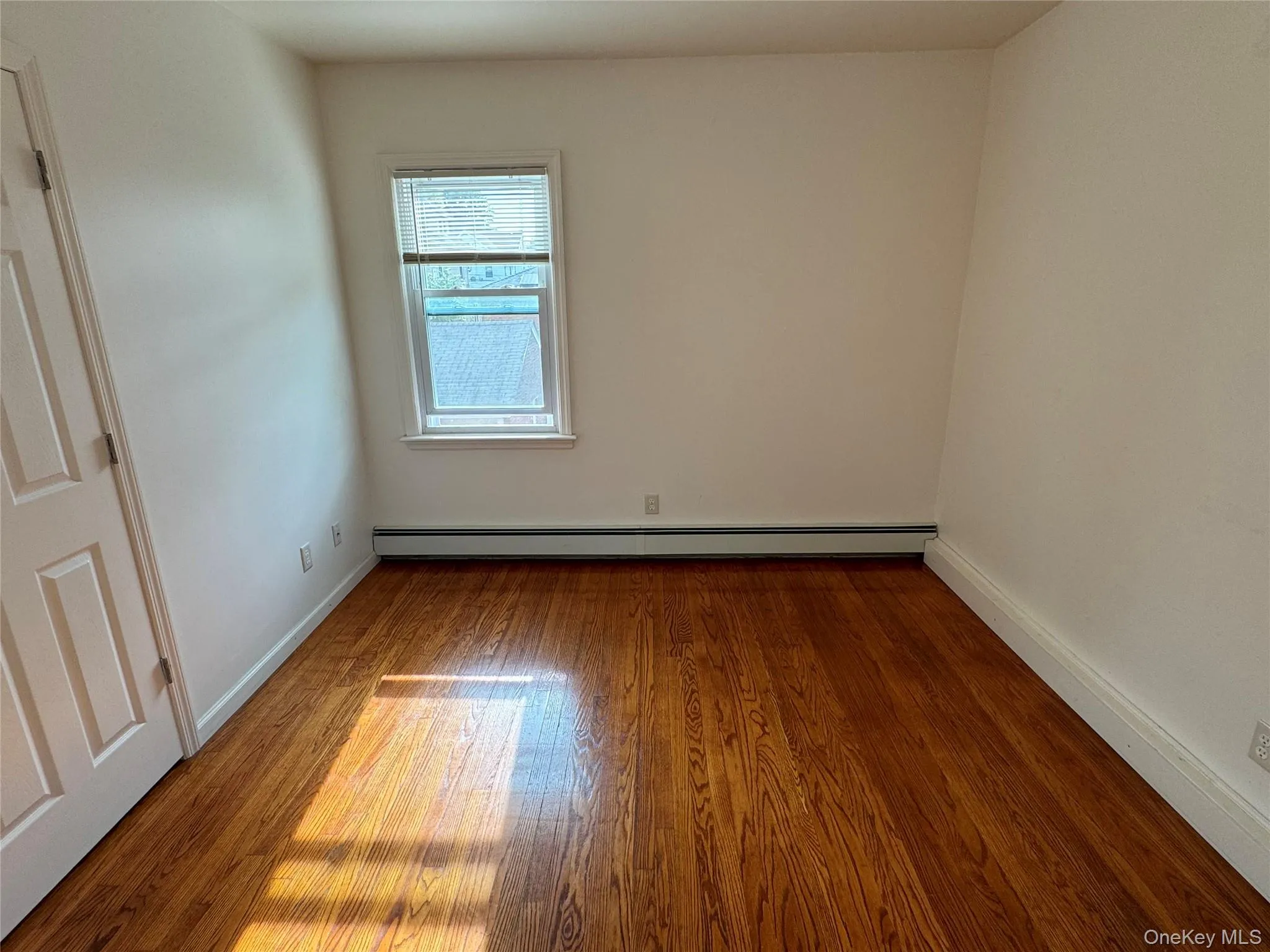 Unfurnished room featuring wood finished floors and a baseboard radiator Unfurnished room featuring wood finished floors and a baseboard radiator