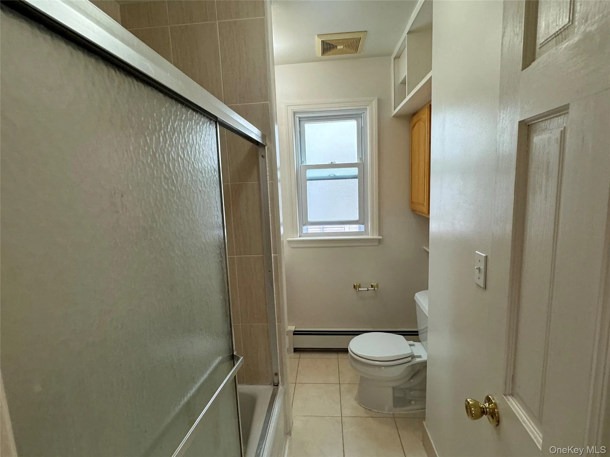 Bathroom featuring light tile patterned floors, a baseboard radiator, and shower / bath combination with glass door Bathroom featuring light tile patterned floors, a baseboard radiator, and shower / bath combination with glass door