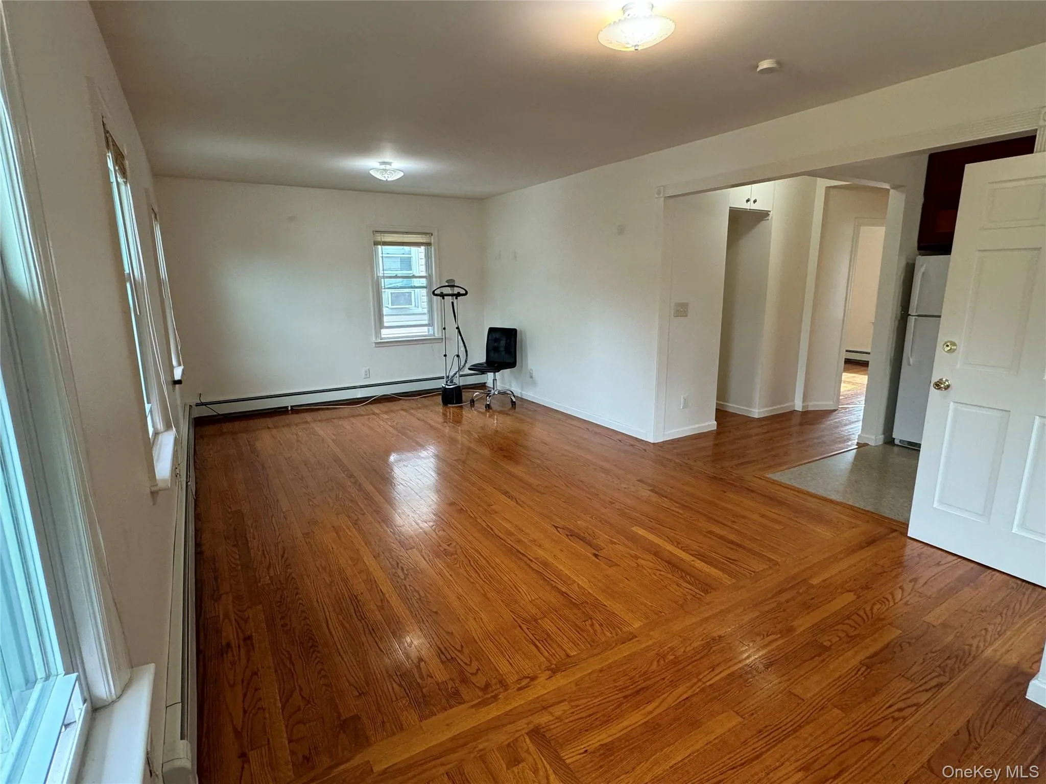 Unfurnished living room featuring light wood-style floors, arched walkways, and a baseboard heating unit Unfurnished living room featuring light wood-style floors, arched walkways, and a baseboard heating unit