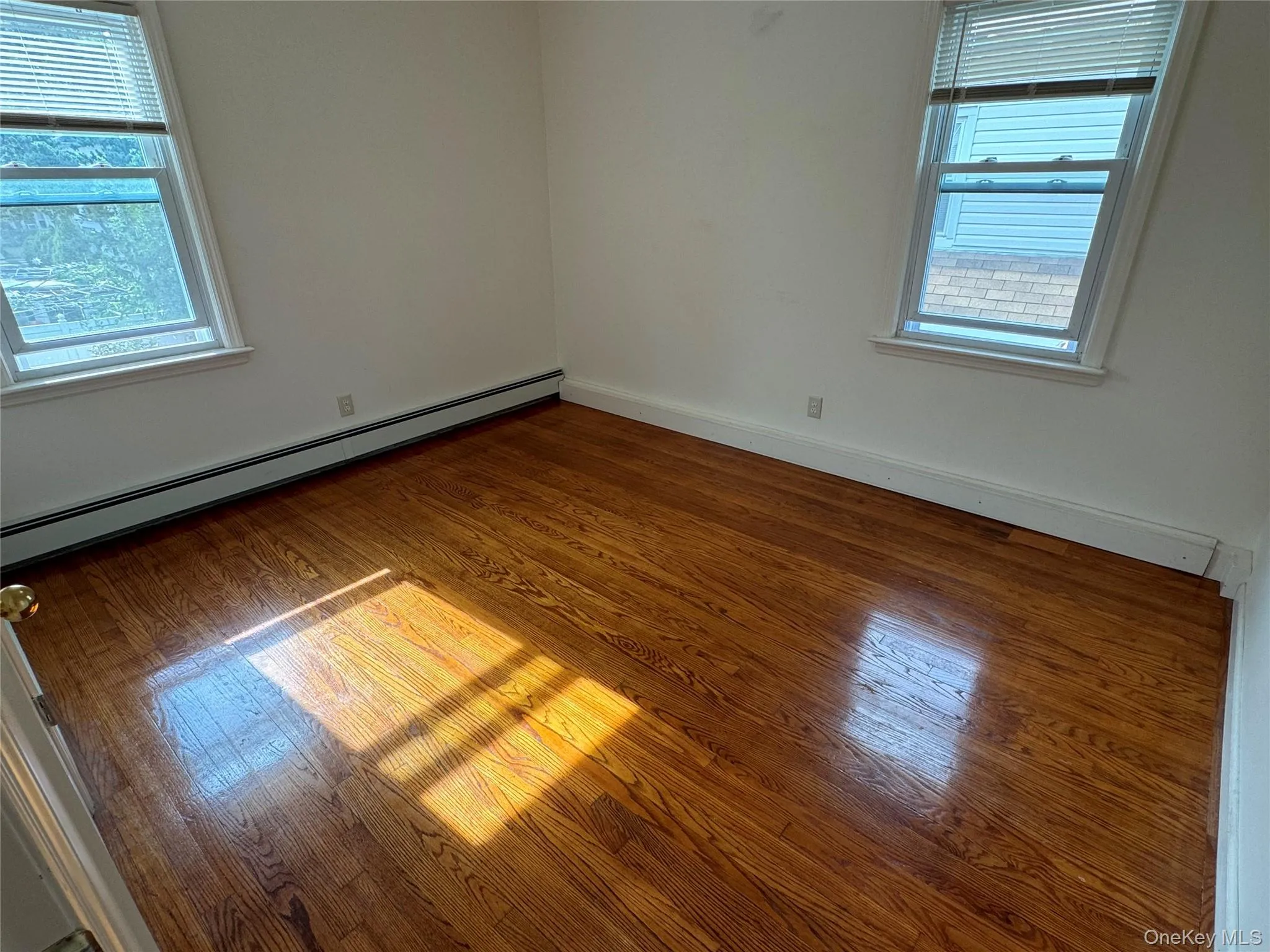 Empty room featuring baseboard heating, plenty of natural light, and hardwood / wood-style floors Empty room featuring baseboard heating, plenty of natural light, and hardwood / wood-style floors