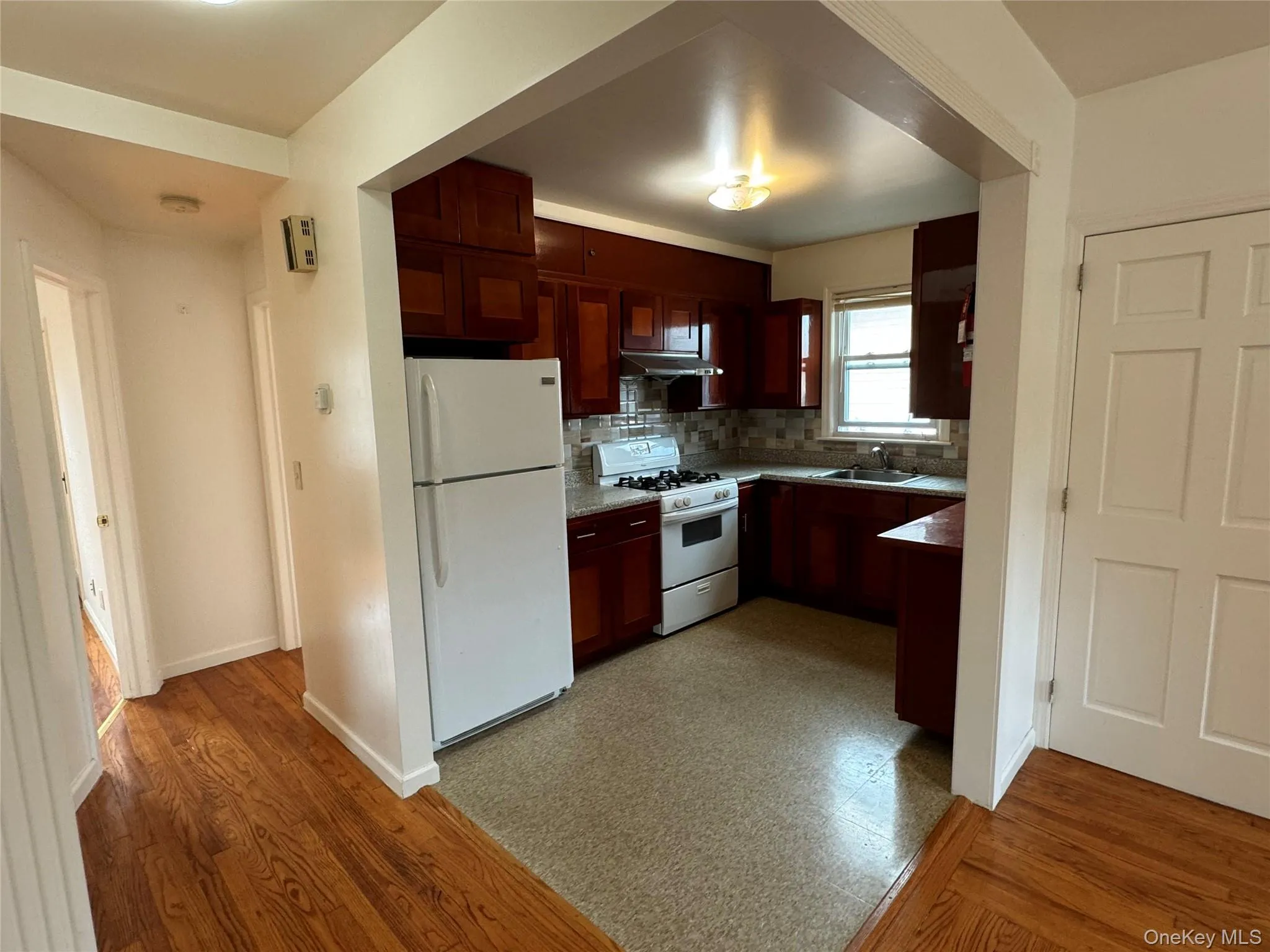 Kitchen featuring tasteful backsplash, white appliances, under cabinet range hood, and light wood-style floors Kitchen featuring tasteful backsplash, white appliances, under cabinet range hood, and light wood-style floors