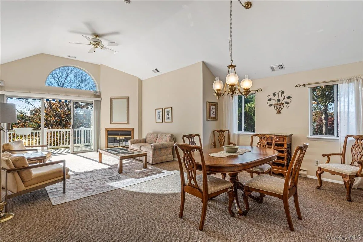 Dining room featuring lofted ceiling, carpet floors, a glass covered fireplace, and a ceiling fan Dining room featuring lofted ceiling, carpet floors, a glass covered fireplace, and a ceiling fan