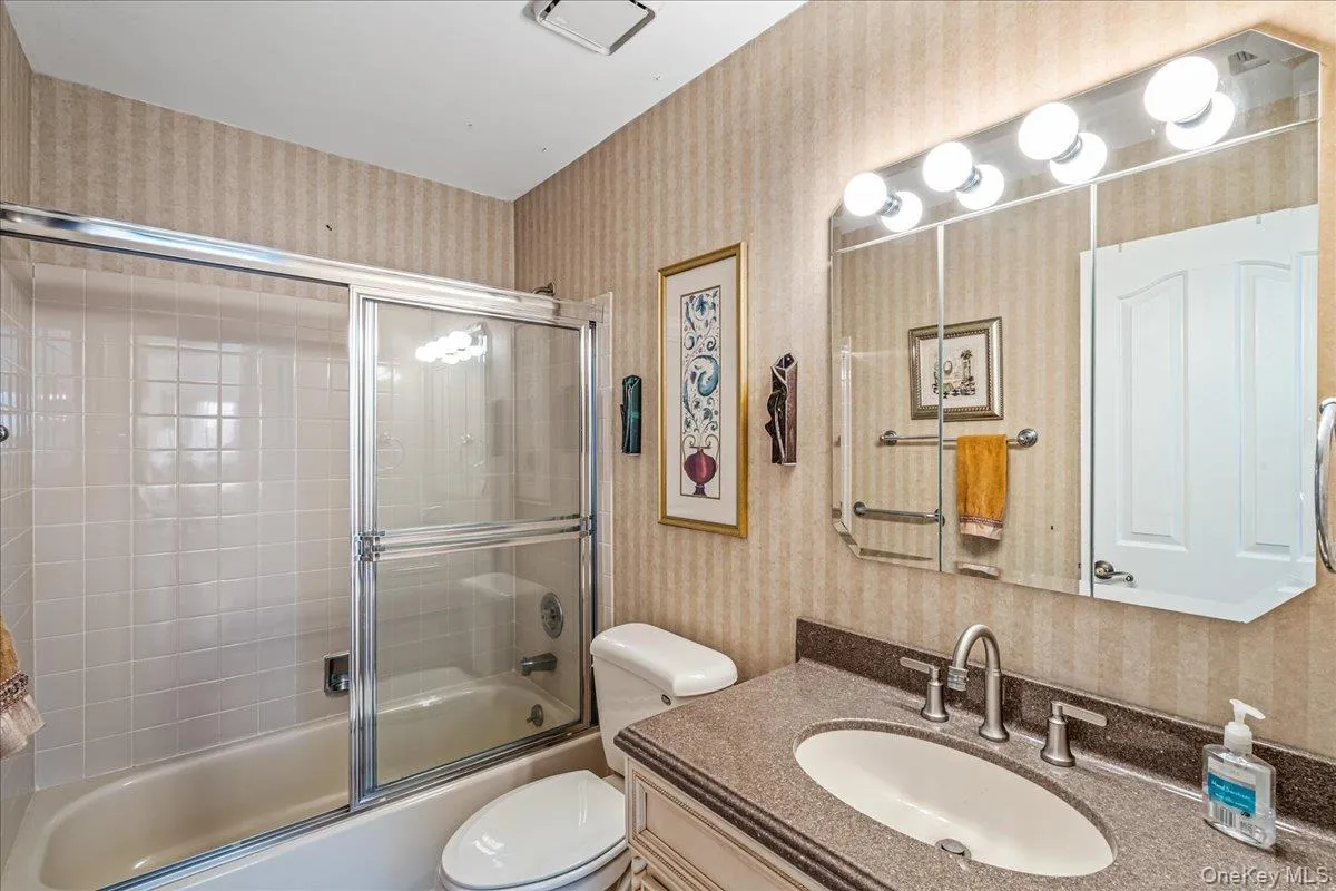 Bathroom featuring wallpapered walls, vanity, and combined bath / shower with glass door Bathroom featuring wallpapered walls, vanity, and combined bath / shower with glass door