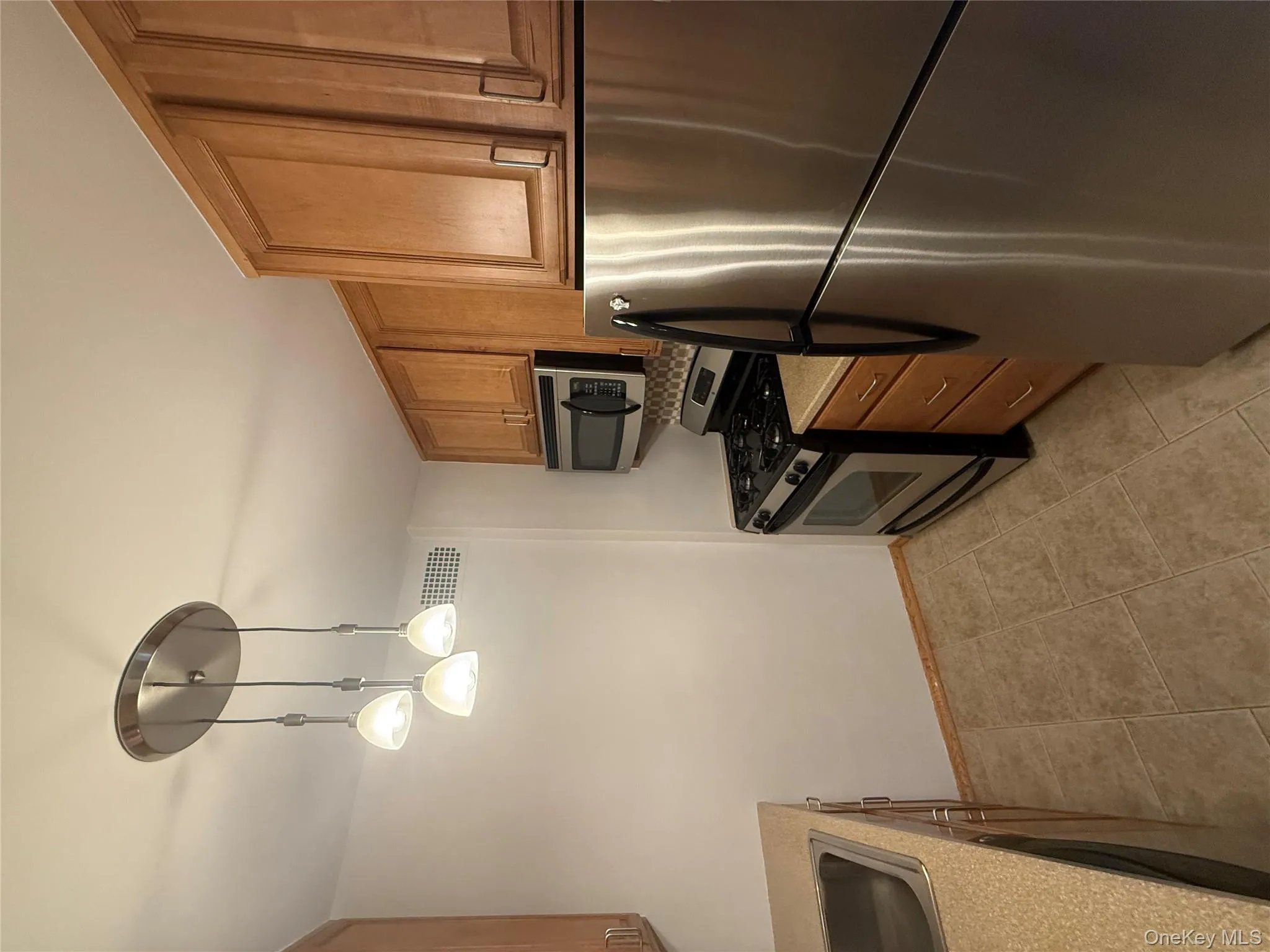 Kitchen featuring appliances with stainless steel finishes, decorative light fixtures, and brown cabinets Kitchen featuring appliances with stainless steel finishes, decorative light fixtures, and brown cabinets