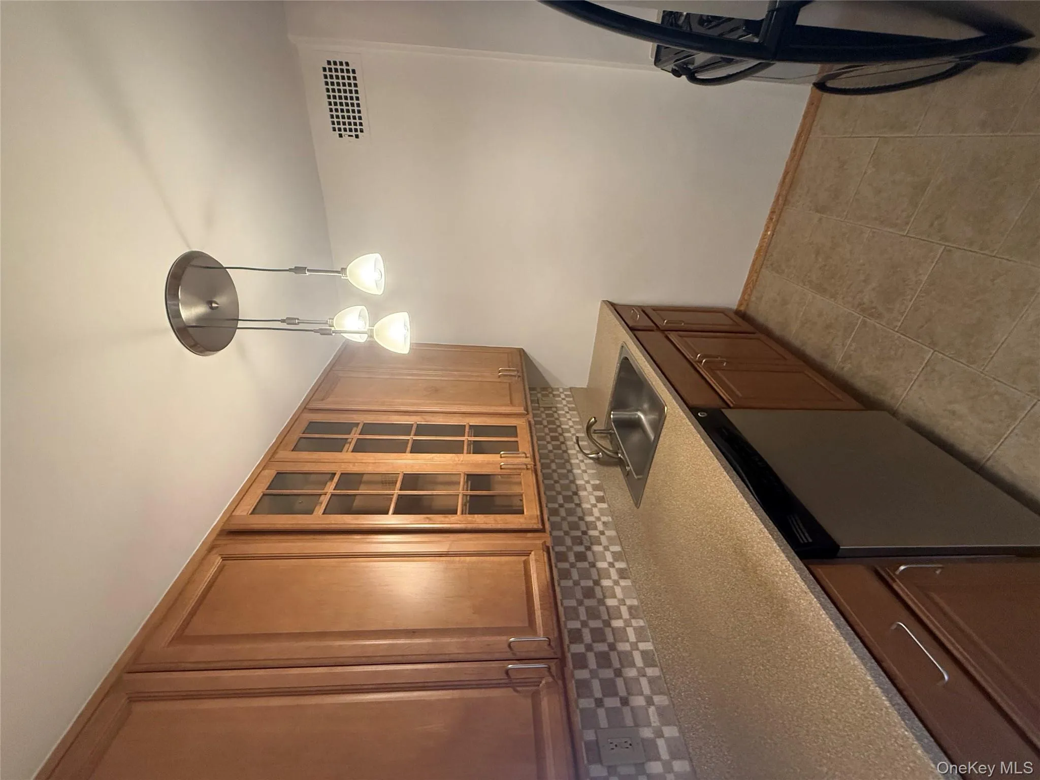 Kitchen with dishwashing machine, glass insert cabinets, decorative backsplash, decorative light fixtures, and brown cabinets Kitchen with dishwashing machine, glass insert cabinets, decorative backsplash, decorative light fixtures, and brown cabinets