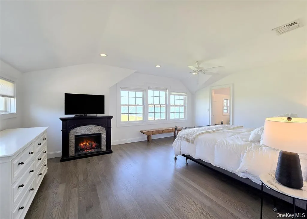 Bedroom with lofted ceiling, dark wood-style flooring, recessed lighting, a warm lit fireplace, and ceiling fan Bedroom with lofted ceiling, dark wood-style flooring, recessed lighting, a warm lit fireplace, and ceiling fan