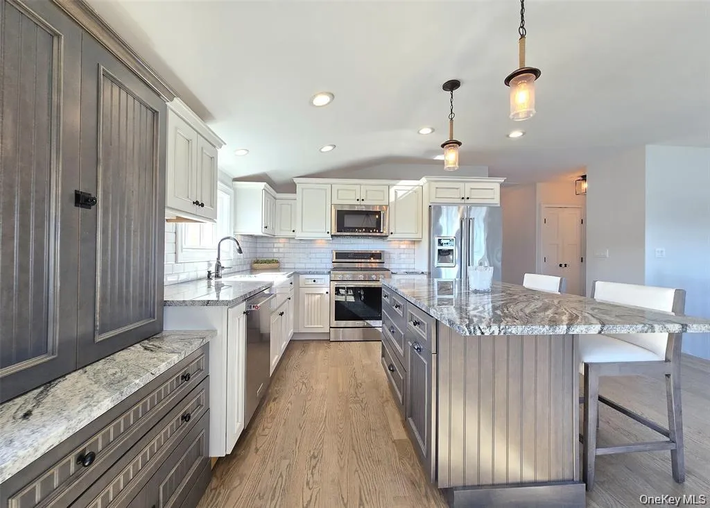 Kitchen featuring a kitchen bar, light stone counters, appliances with stainless steel finishes, decorative light fixtures, and light wood-style floors Kitchen featuring a kitchen bar, light stone counters, appliances with stainless steel finishes, decorative light fixtures, and light wood-style floors