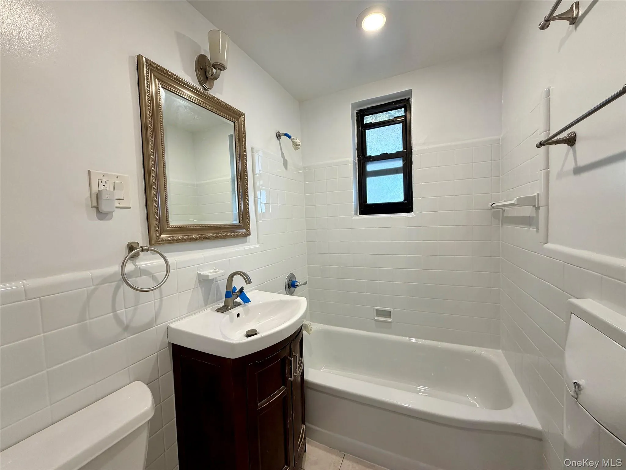 Bathroom with tile walls, vanity, tub / shower combination, and a wainscoted wall Bathroom with tile walls, vanity, tub / shower combination, and a wainscoted wall