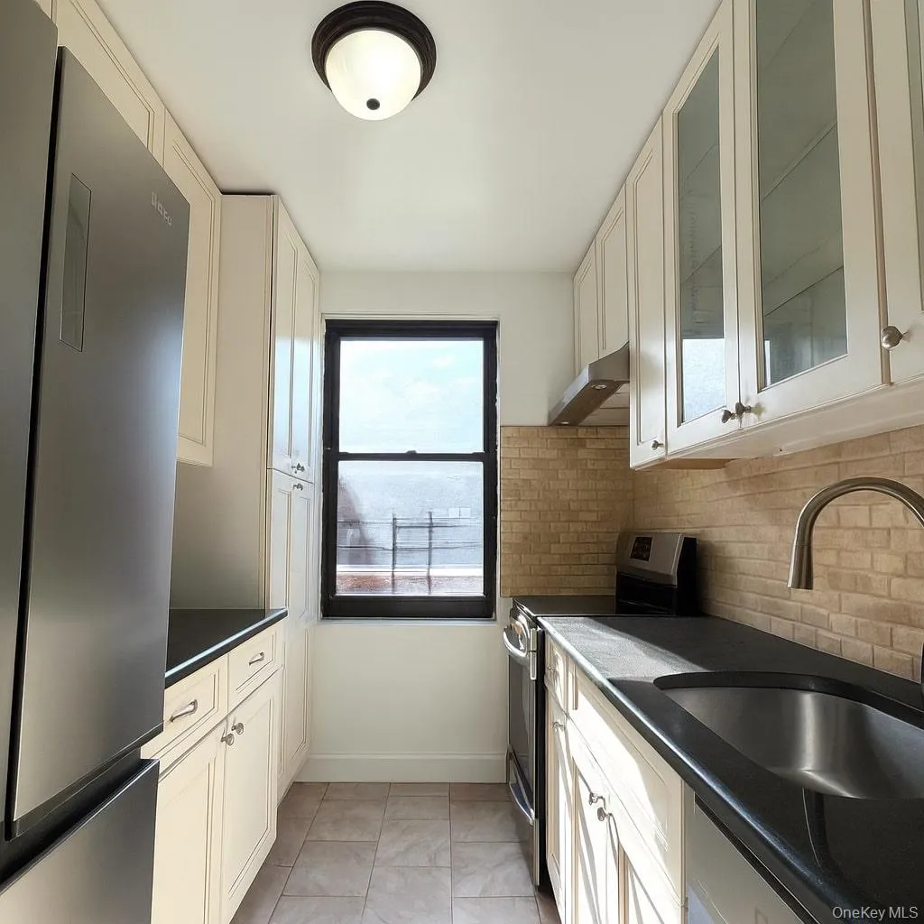 Kitchen with appliances with stainless steel finishes, glass insert cabinets, light tile patterned floors, white cabinets, and under cabinet range hood Kitchen with appliances with stainless steel finishes, glass insert cabinets, light tile patterned floors, white cabinets, and under cabinet range hood