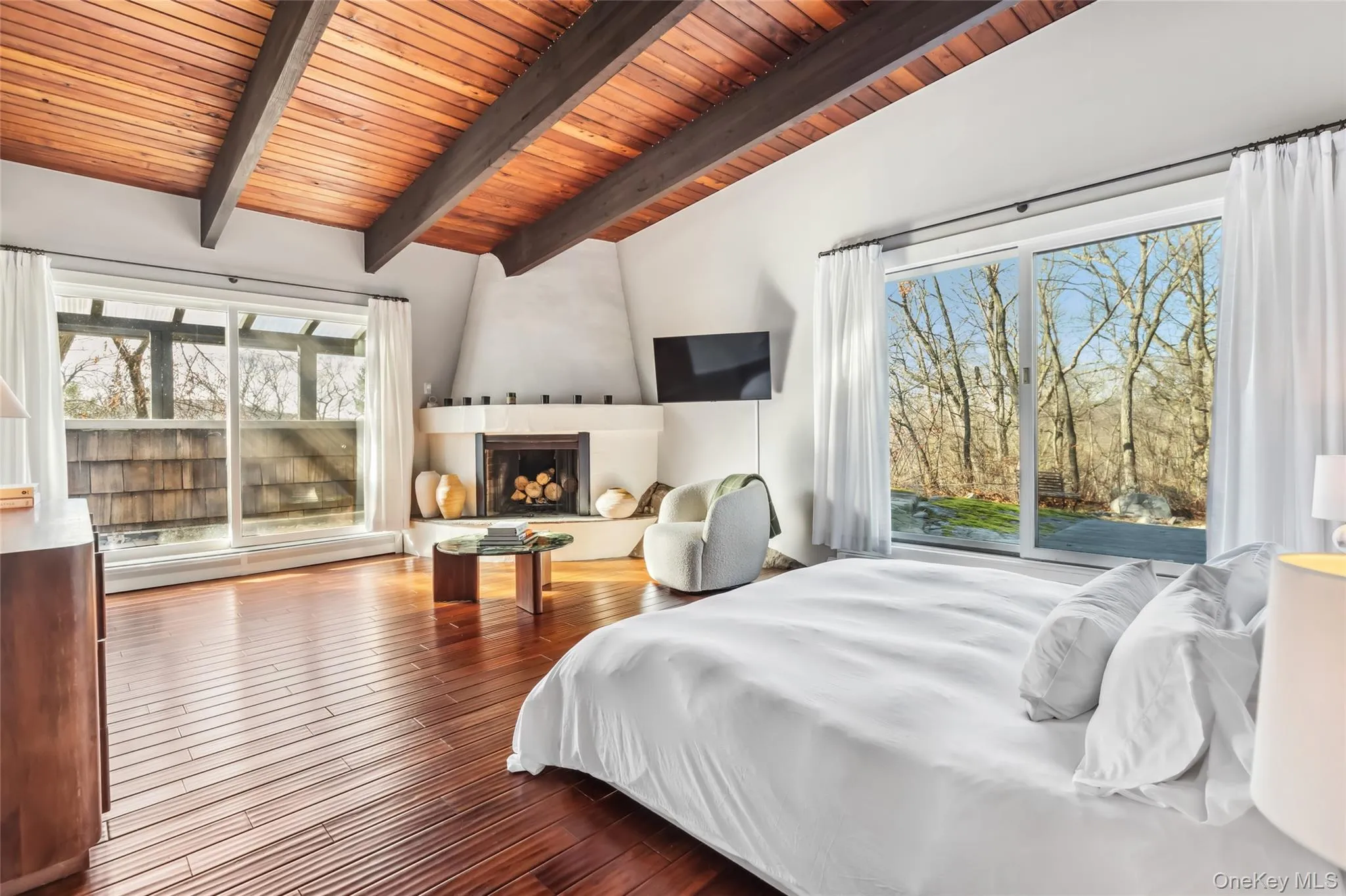 Bedroom with a large fireplace, baseboard heating, vaulted ceiling with beams, wood-type flooring, and wood ceiling Bedroom with a large fireplace, baseboard heating, vaulted ceiling with beams, wood-type flooring, and wood ceiling