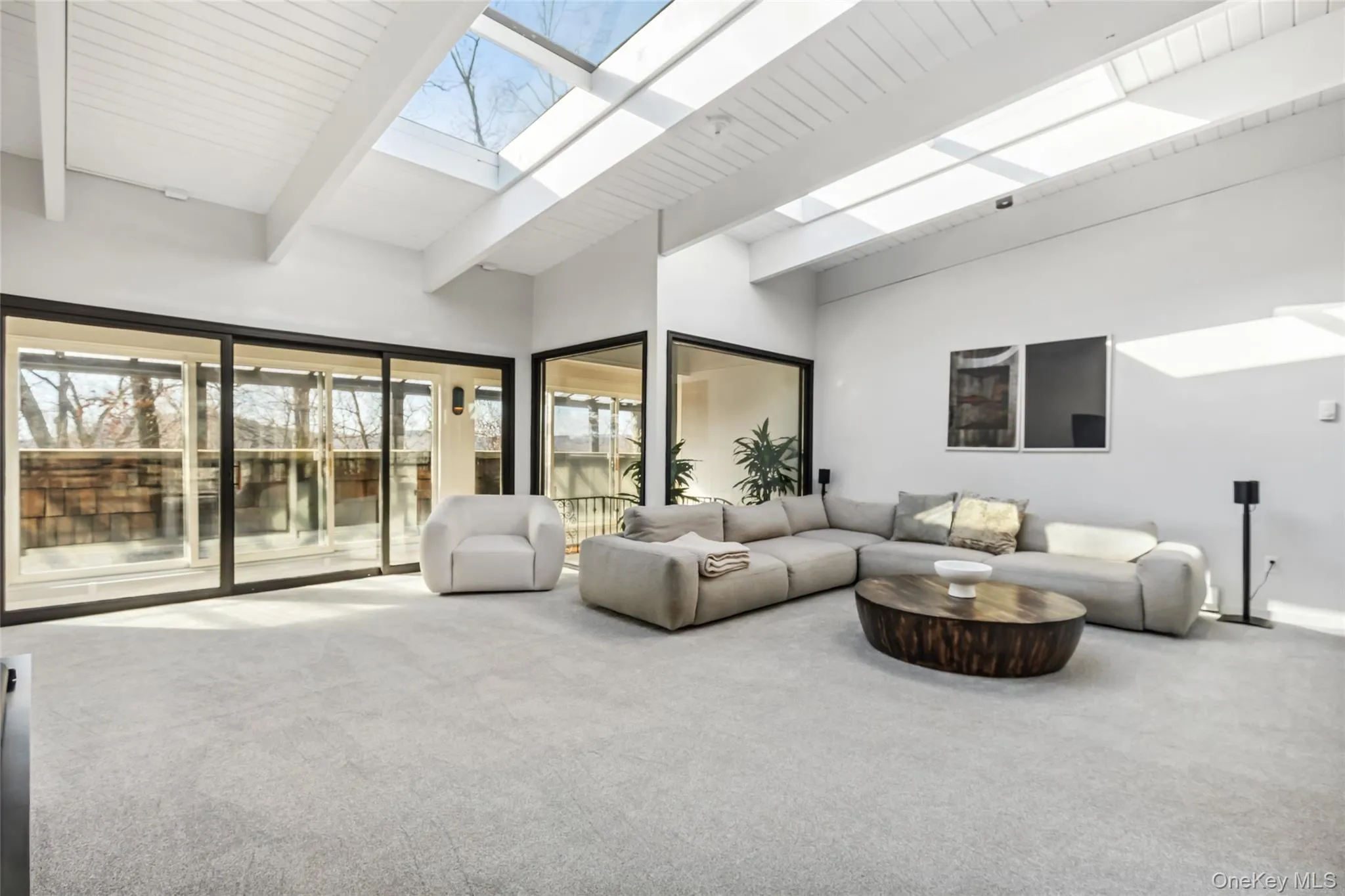 Carpeted living room with beam ceiling, a towering ceiling, a skylight, and plenty of natural light Carpeted living room with beam ceiling, a towering ceiling, a skylight, and plenty of natural light