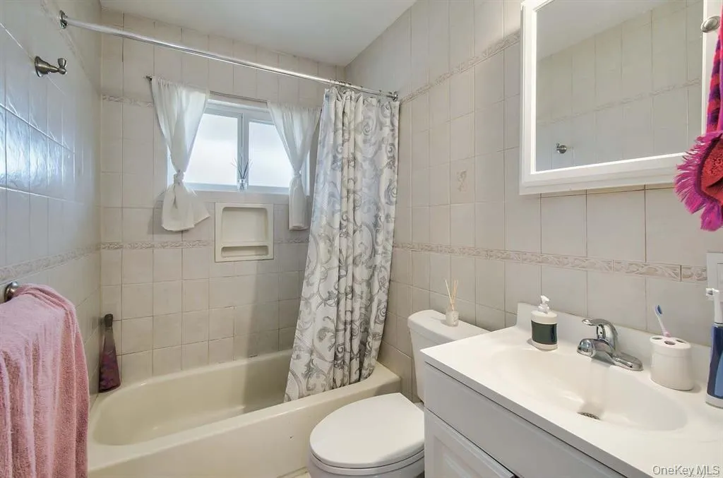 Full bath featuring vanity, tile walls, and shower / bathtub combination with curtain Full bath featuring vanity, tile walls, and shower / bathtub combination with curtain