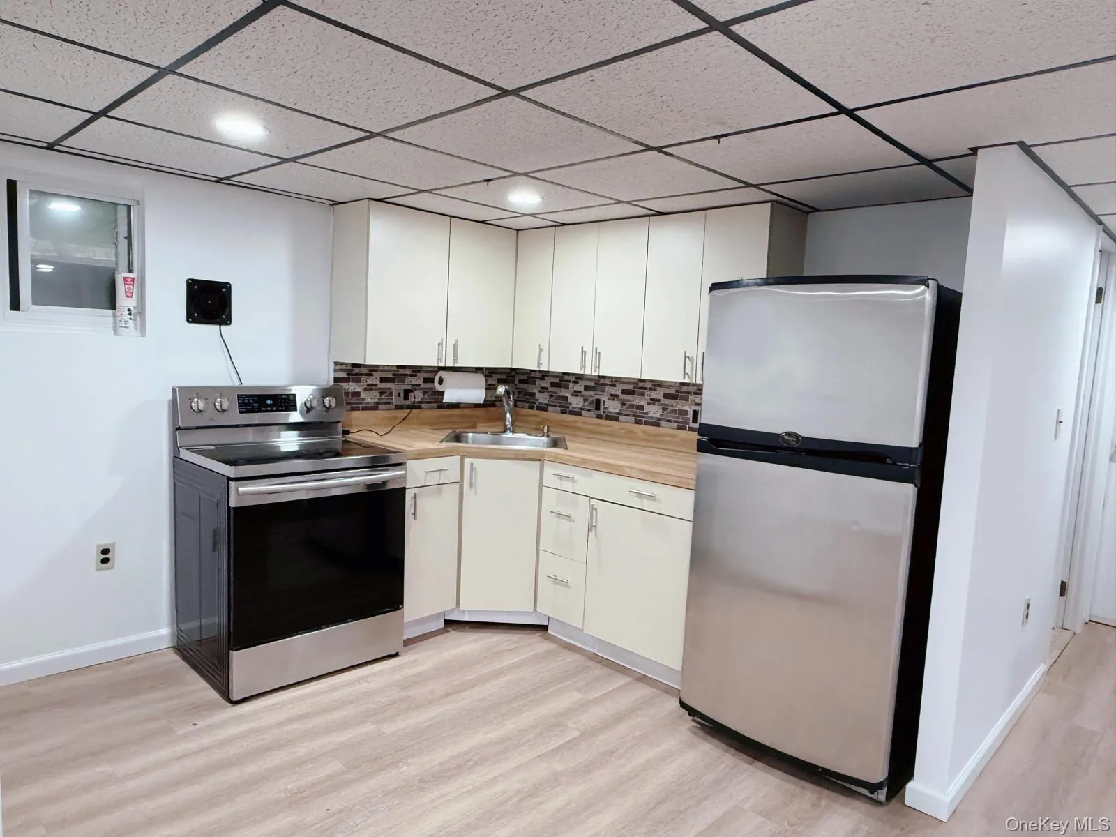 Kitchen featuring appliances with stainless steel finishes, light countertops, backsplash, a paneled ceiling, and light wood-type flooring Kitchen featuring appliances with stainless steel finishes, light countertops, backsplash, a paneled ceiling, and light wood-type flooring