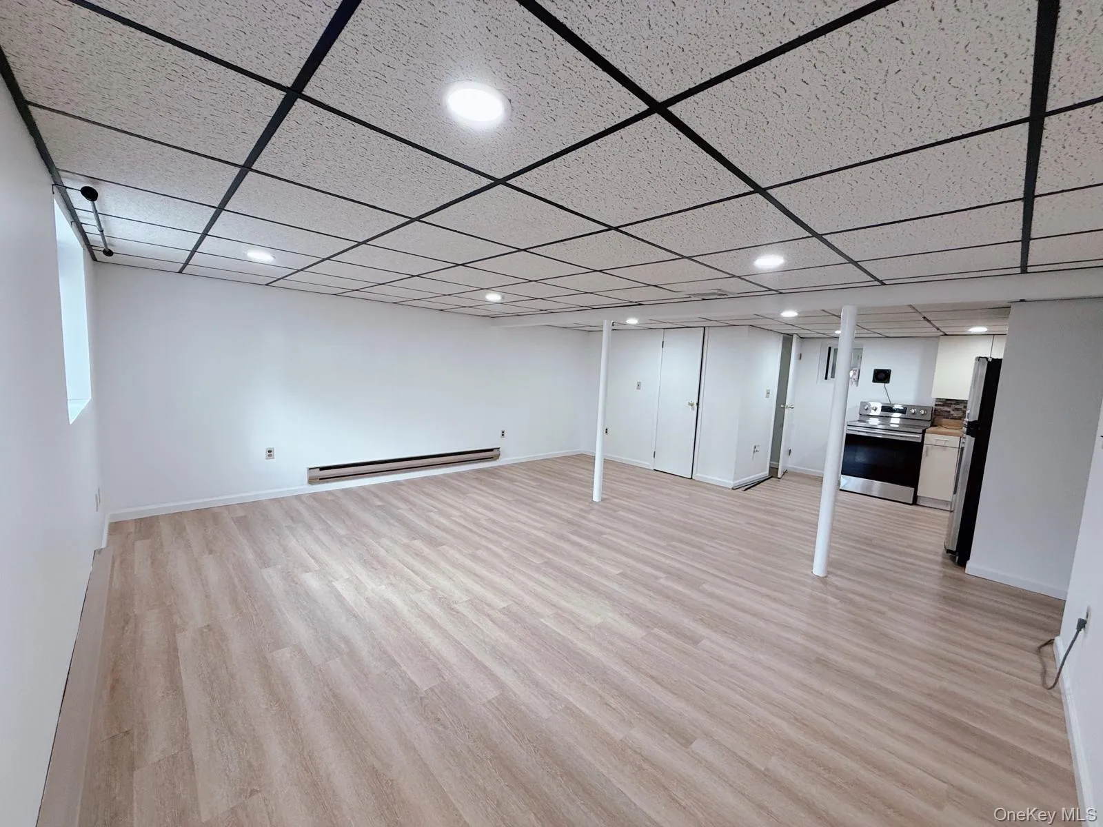 Finished below grade area with light wood-style floors, freestanding refrigerator, recessed lighting, a baseboard radiator, and a paneled ceiling Finished below grade area with light wood-style floors, freestanding refrigerator, recessed lighting, a baseboard radiator, and a paneled ceiling