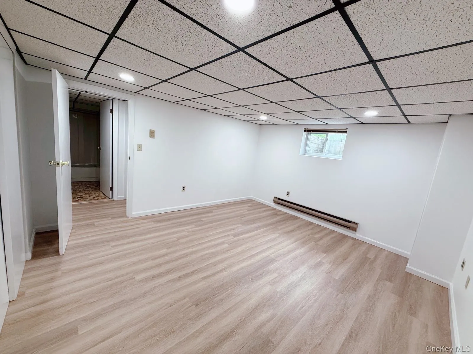 Below grade area featuring light wood finished floors, a baseboard heating unit, recessed lighting, and a paneled ceiling Below grade area featuring light wood finished floors, a baseboard heating unit, recessed lighting, and a paneled ceiling