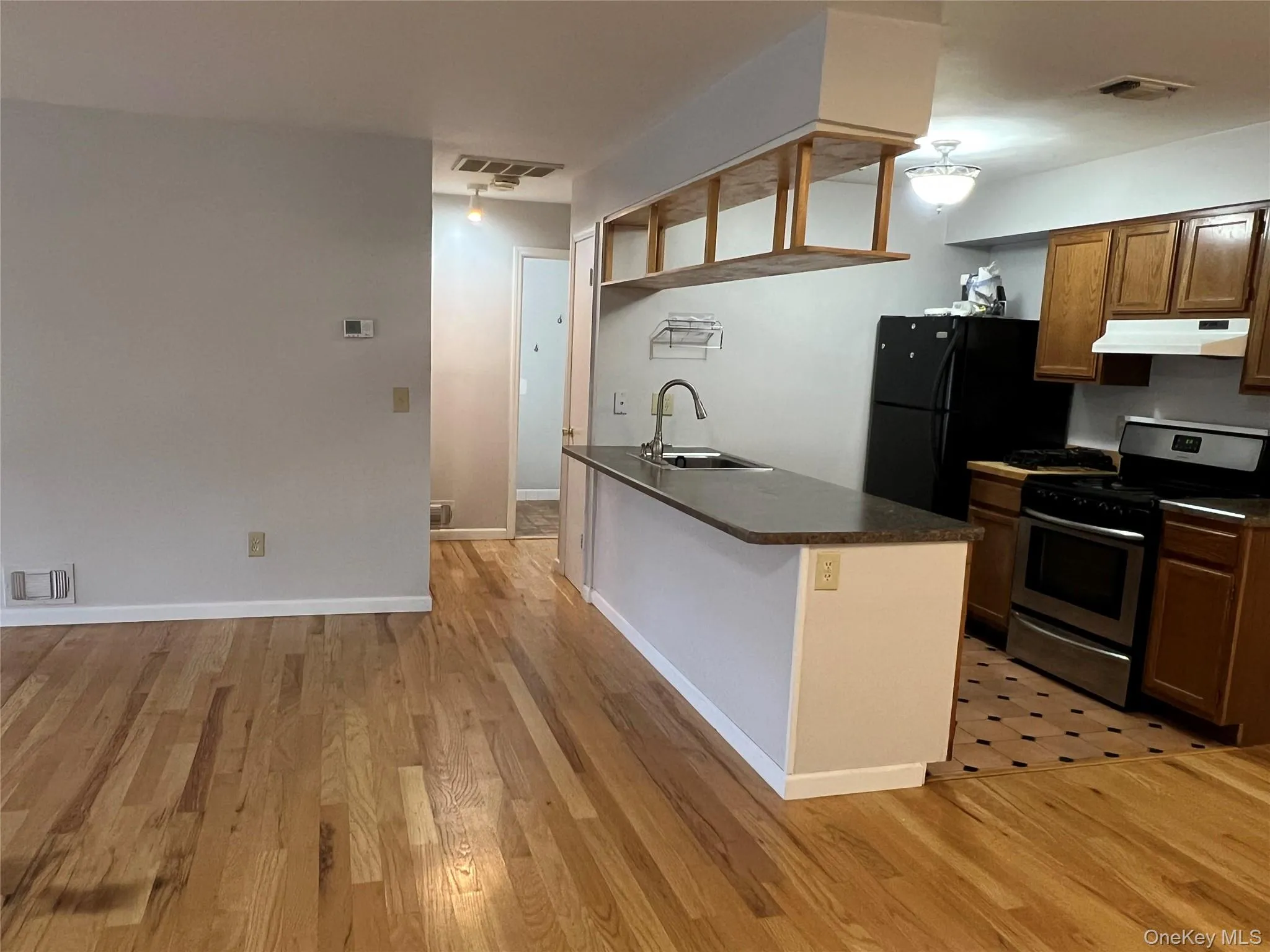Kitchen featuring dark countertops, stainless steel gas stove, light wood-type flooring, and under cabinet range hood Kitchen featuring dark countertops, stainless steel gas stove, light wood-type flooring, and under cabinet range hood