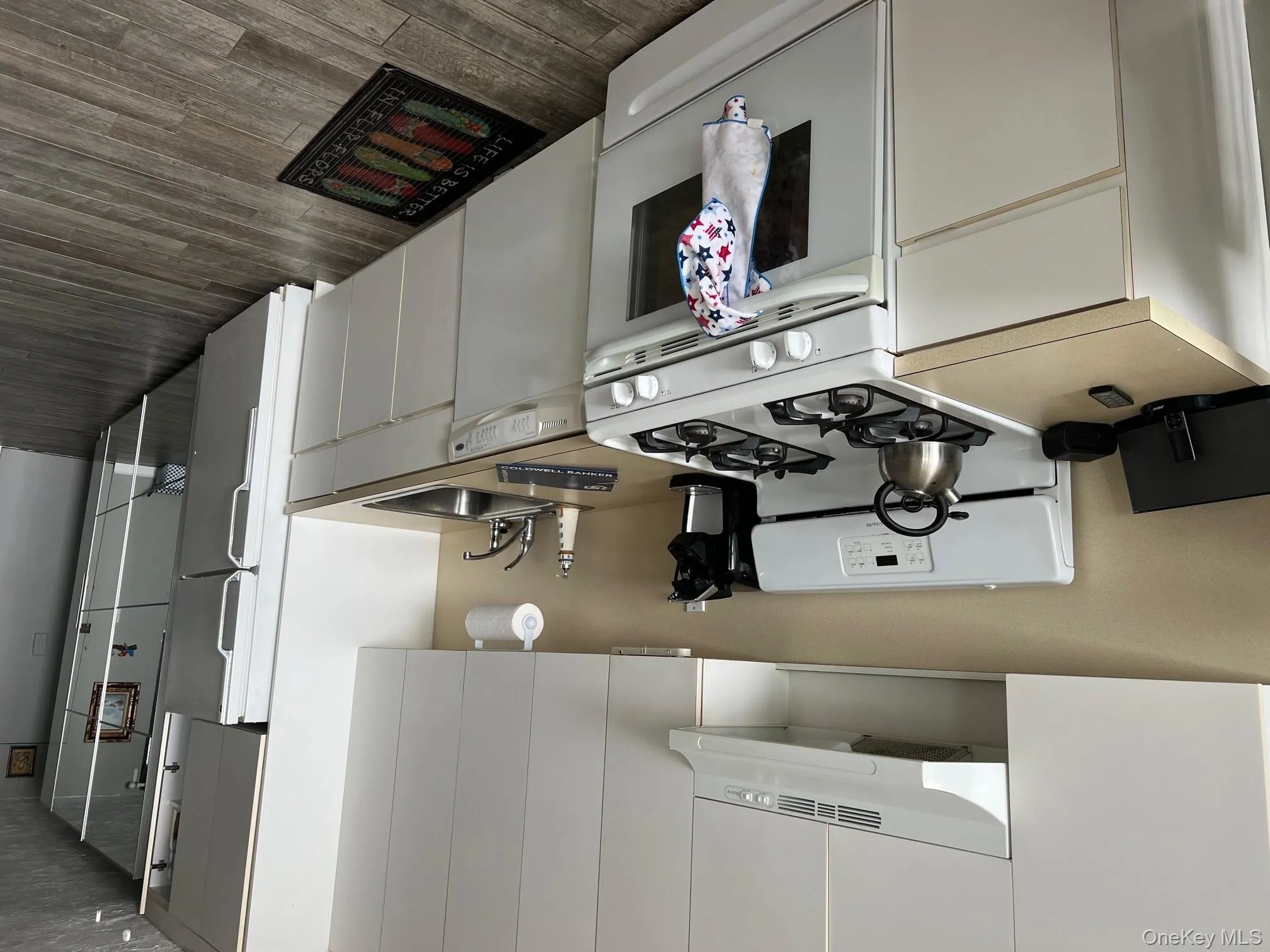 Kitchen featuring white appliances, exhaust hood, light countertops, and white cabinetry Kitchen featuring white appliances, exhaust hood, light countertops, and white cabinetry