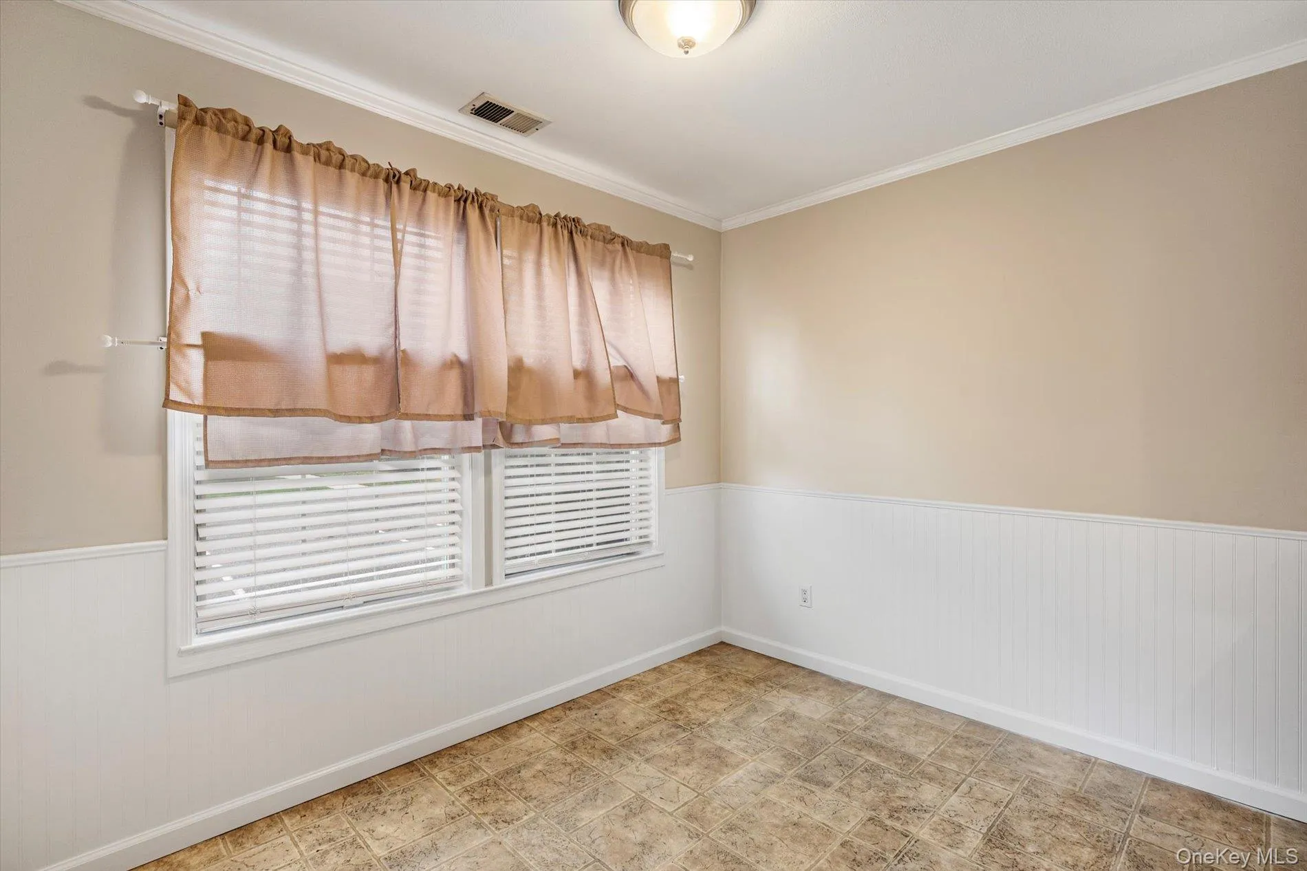 Empty room featuring a wainscoted wall and ornamental molding Empty room featuring a wainscoted wall and ornamental molding
