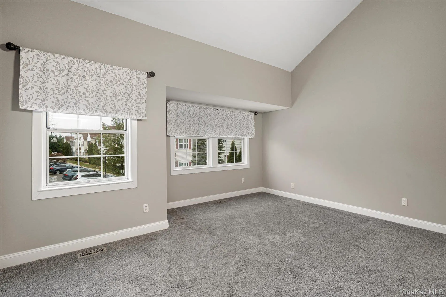 Carpeted empty room with vaulted ceiling and baseboards Carpeted empty room with vaulted ceiling and baseboards