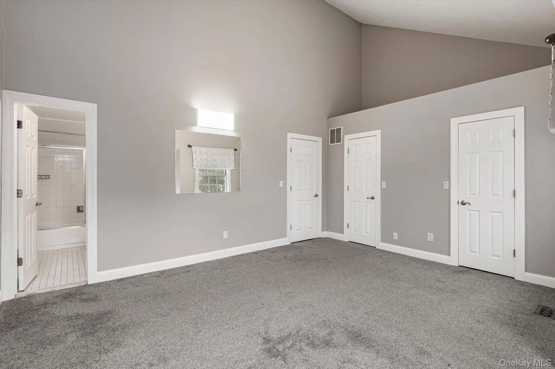 Unfurnished bedroom with high vaulted ceiling, carpet flooring, and ensuite bathroom Unfurnished bedroom with high vaulted ceiling, carpet flooring, and ensuite bathroom