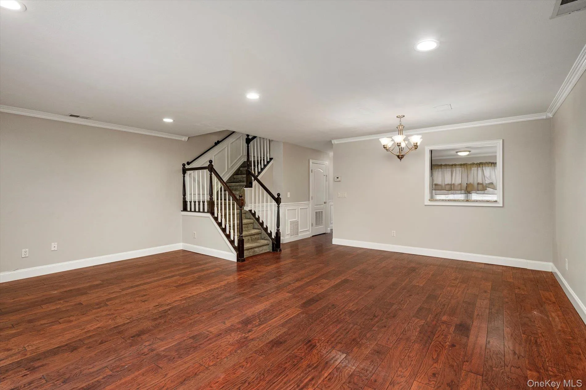 Unfurnished living room with stairs, crown molding, dark wood-style floors, recessed lighting, and a chandelier Unfurnished living room with stairs, crown molding, dark wood-style floors, recessed lighting, and a chandelier