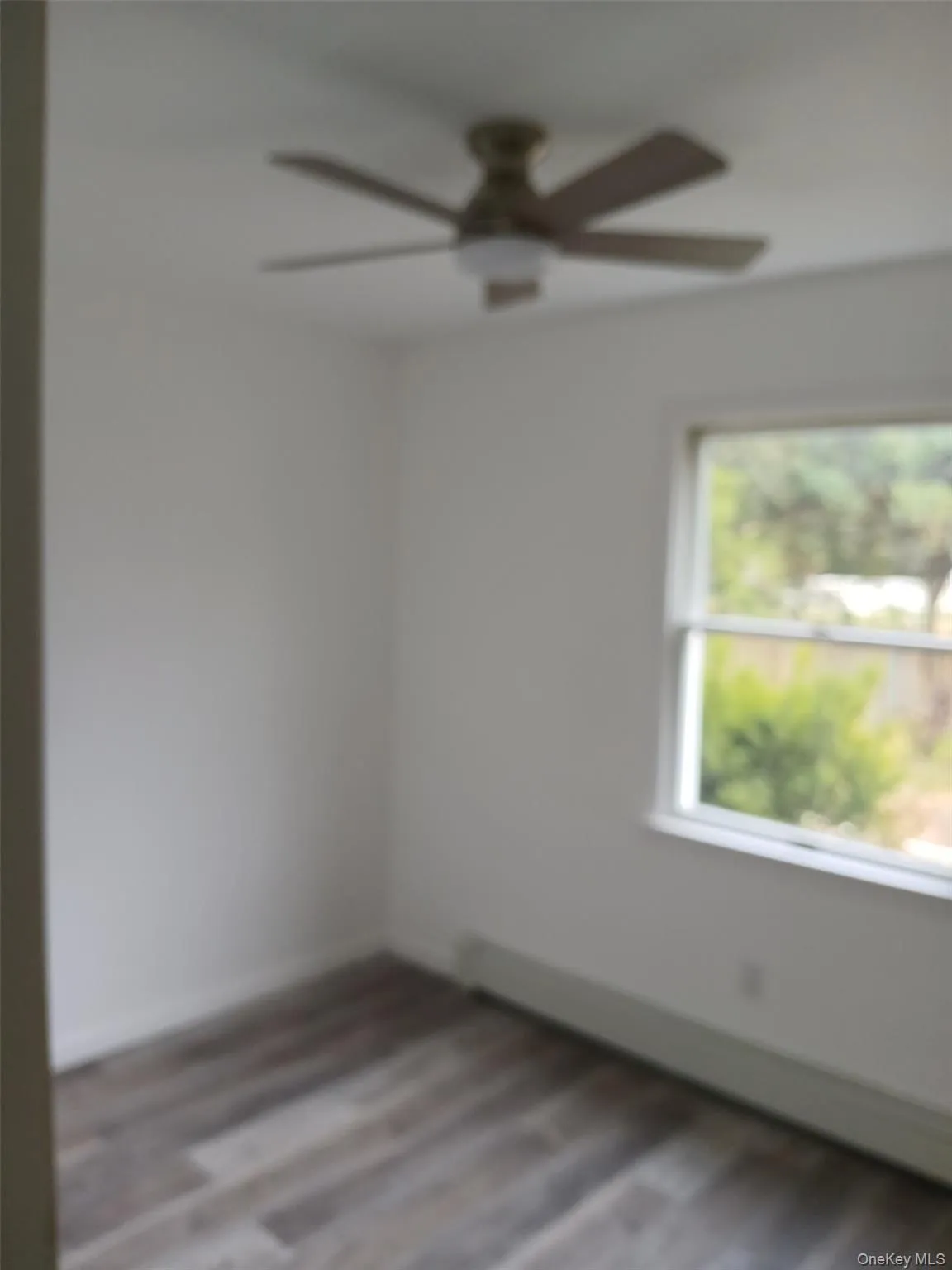 Empty room with dark wood finished floors, baseboard heating, and a ceiling fan Empty room with dark wood finished floors, baseboard heating, and a ceiling fan