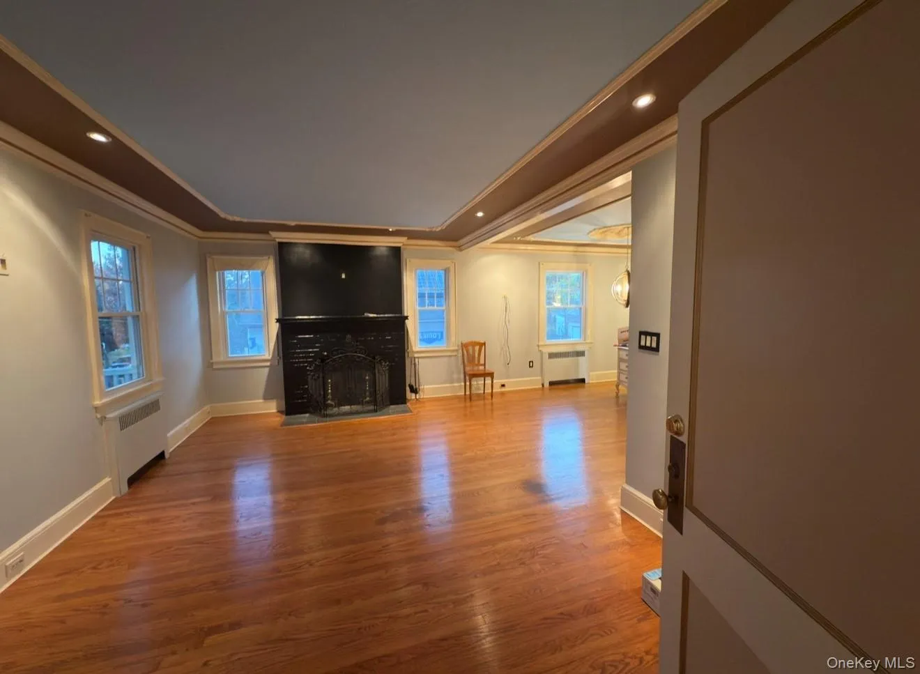 Unfurnished living room with crown molding, light wood-type flooring, radiator heating unit, recessed lighting, and healthy amount of natural light Unfurnished living room with crown molding, light wood-type flooring, radiator heating unit, recessed lighting, and healthy amount of natural light