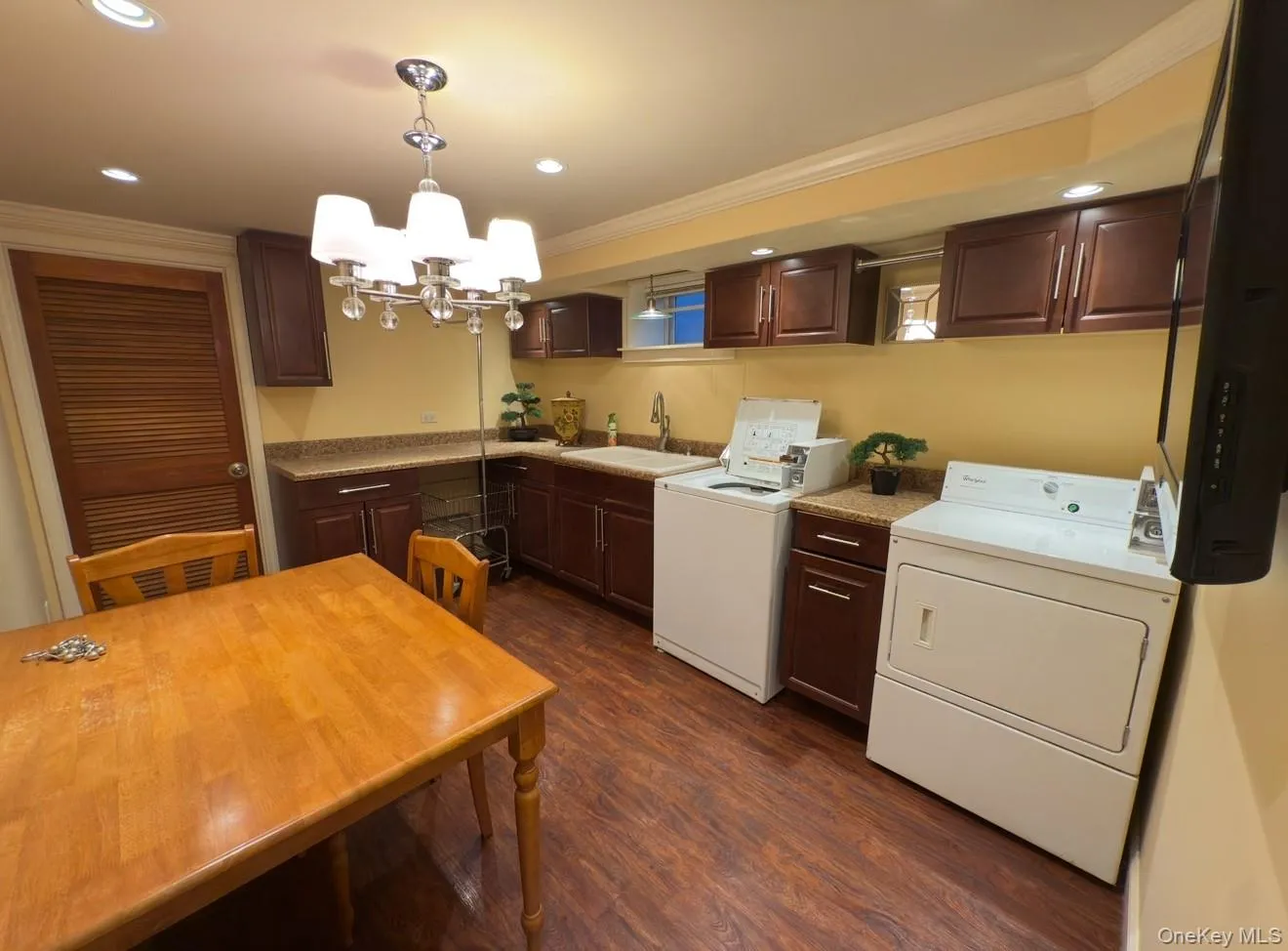 Basement laundry dark wood-style flooring, a chandelier, ornamental molding, dark brown cabinetry, and light countertops Basement laundry dark wood-style flooring, a chandelier, ornamental molding, dark brown cabinetry, and light countertops