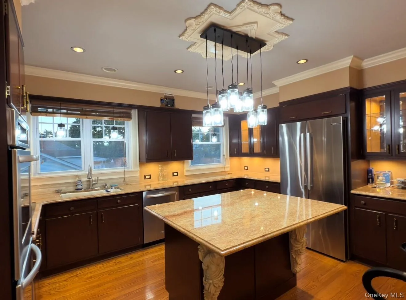 Kitchen featuring a center island, glass insert cabinets, dark brown cabinets, light wood-style floors, and appliances with stainless steel finishes Kitchen featuring a center island, glass insert cabinets, dark brown cabinets, light wood-style floors, and appliances with stainless steel finishes