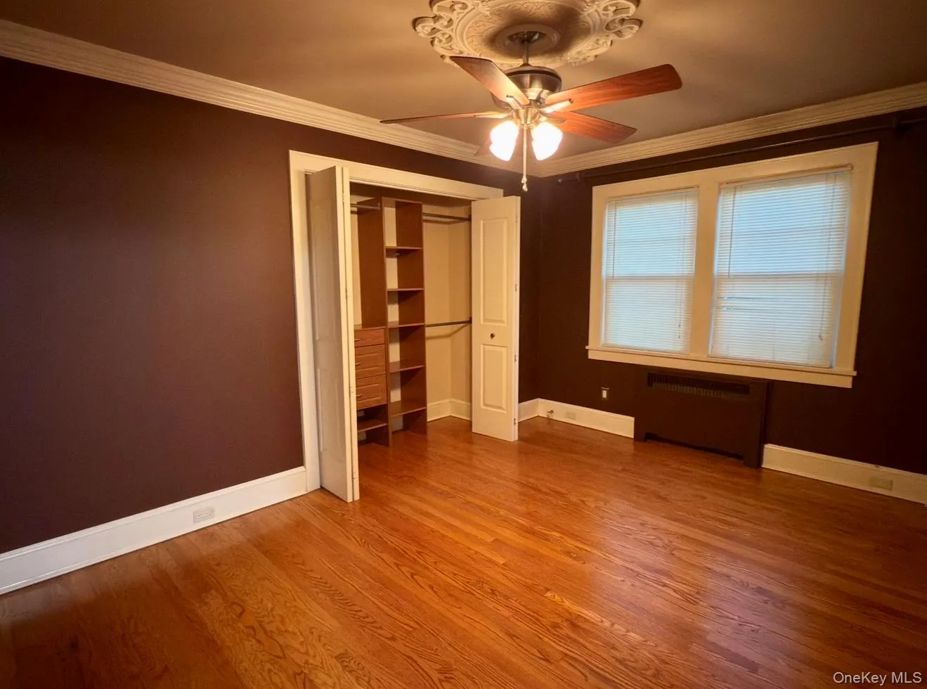 Unfurnished bedroom with crown molding, radiator heating unit, light wood finished floors, a ceiling fan, and a closet Unfurnished bedroom with crown molding, radiator heating unit, light wood finished floors, a ceiling fan, and a closet