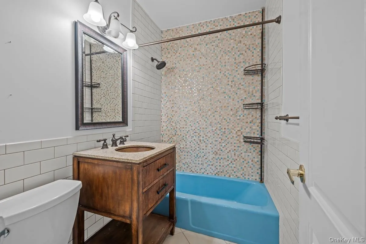 Full bath with tile walls, washtub / shower combination, vanity, and a wainscoted wall Full bath with tile walls, washtub / shower combination, vanity, and a wainscoted wall